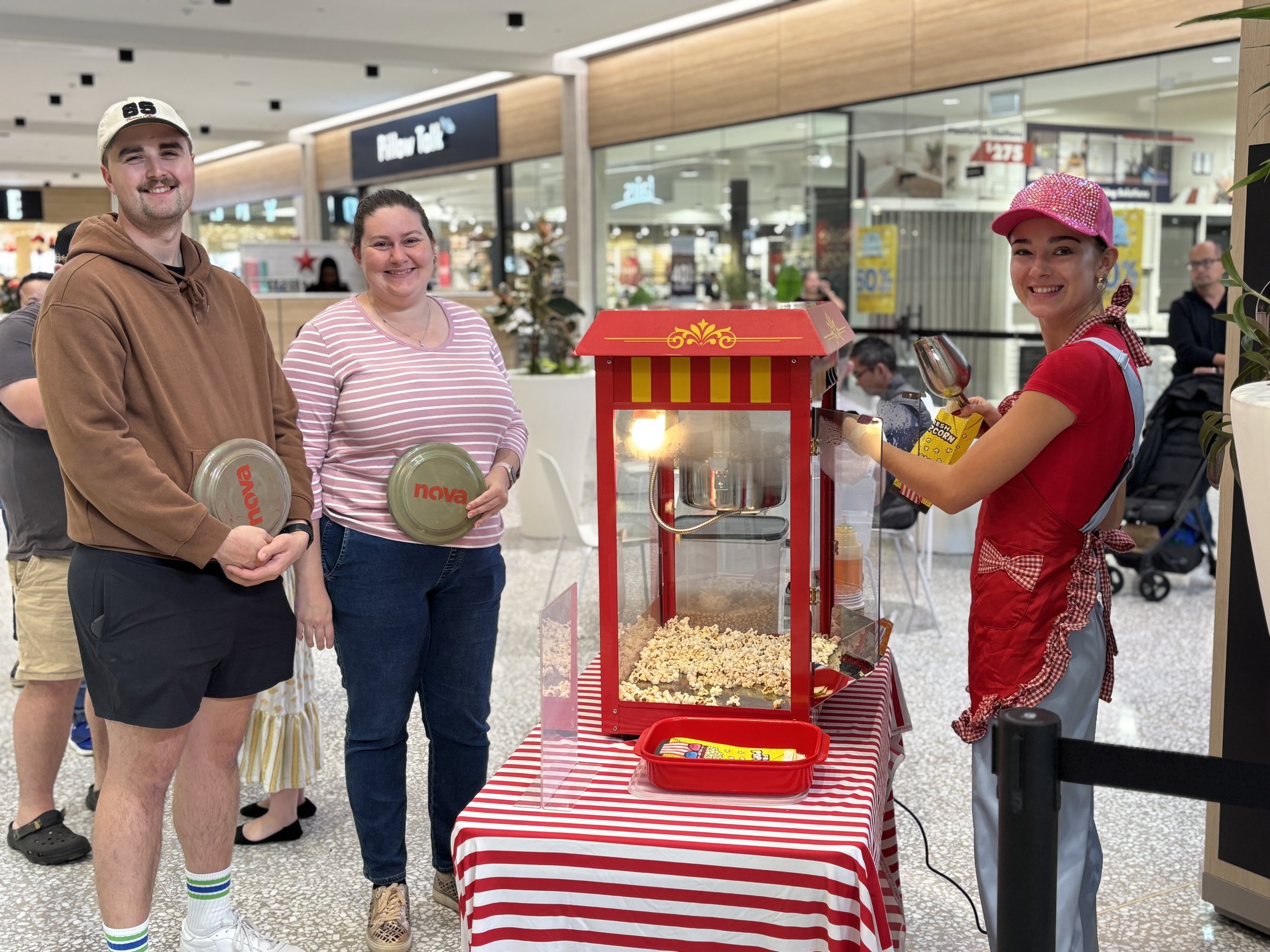 Event staff member serving fresh popcorn next to red popcorn machine on striped table