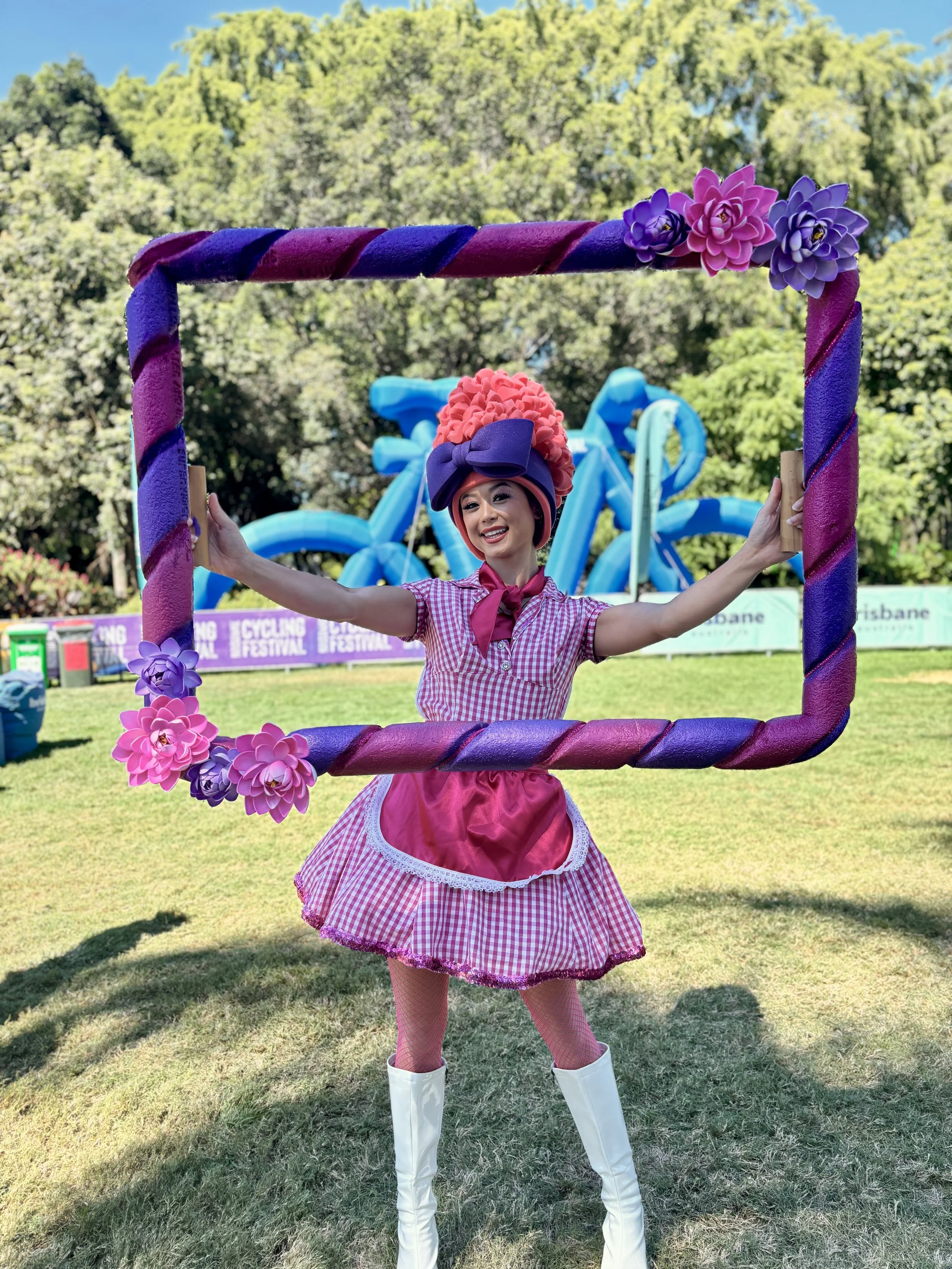 Roving performer interacting with guests using a custom pink and purple picture frame at an outdoor festival event in Brisbane