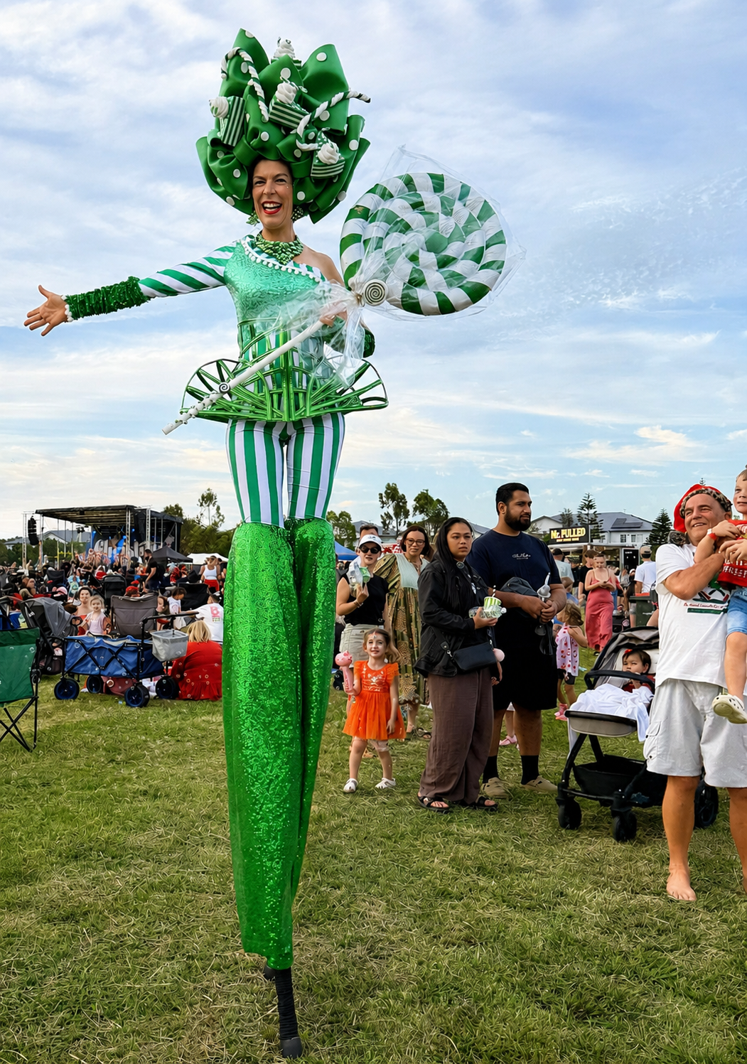 Green stilt walker performing at an outdoor family festival in Brisbane.
