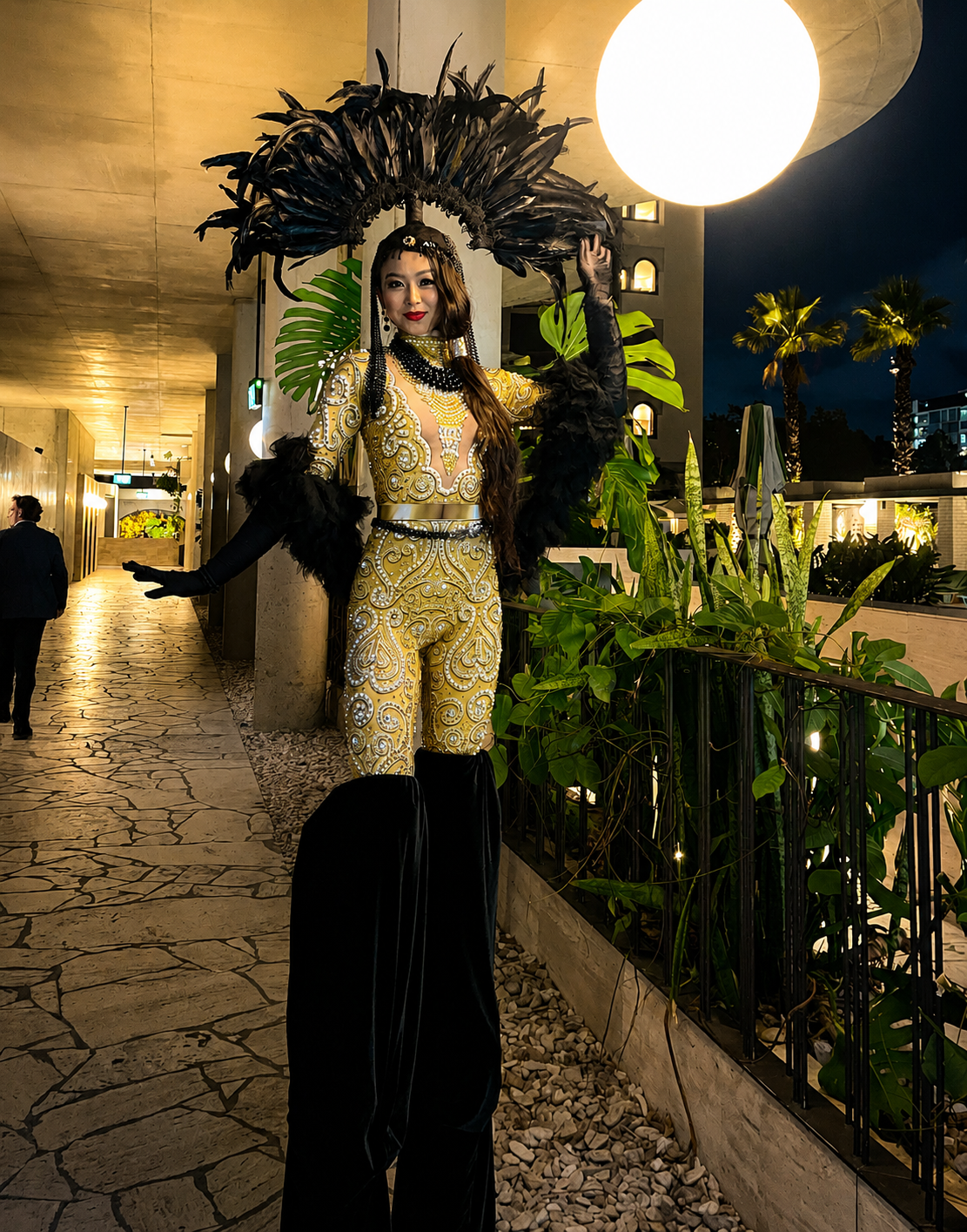 Elegant black and gold showgirl stilt walker performing at a luxury evening event.