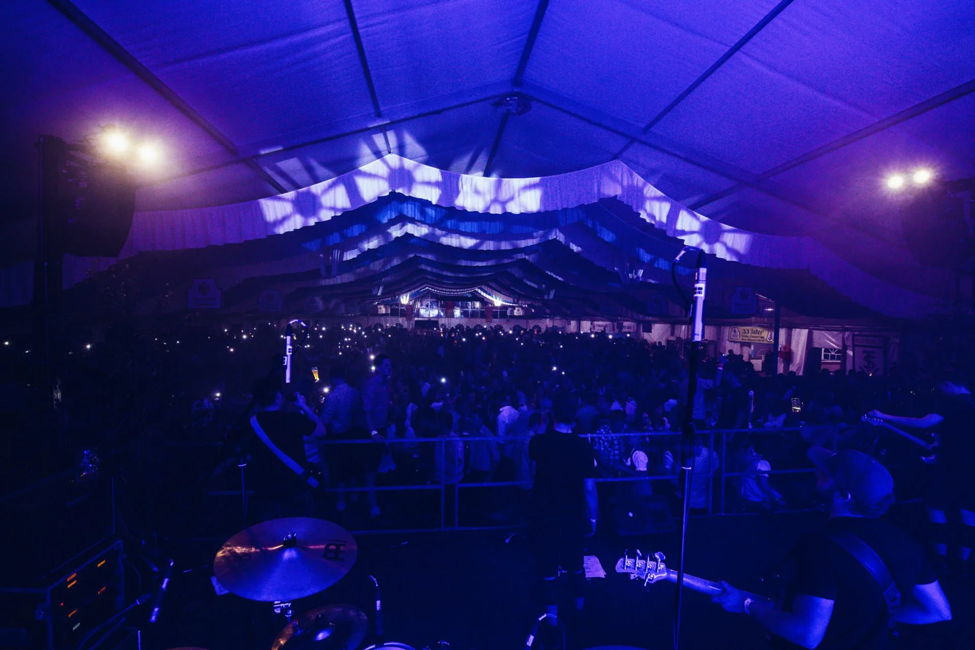 Blick auf eine große Menschenmenge in einer Zeltveranstaltung mit blauer Beleuchtung und Musikern auf der Bühne, Szene bei Nacht.