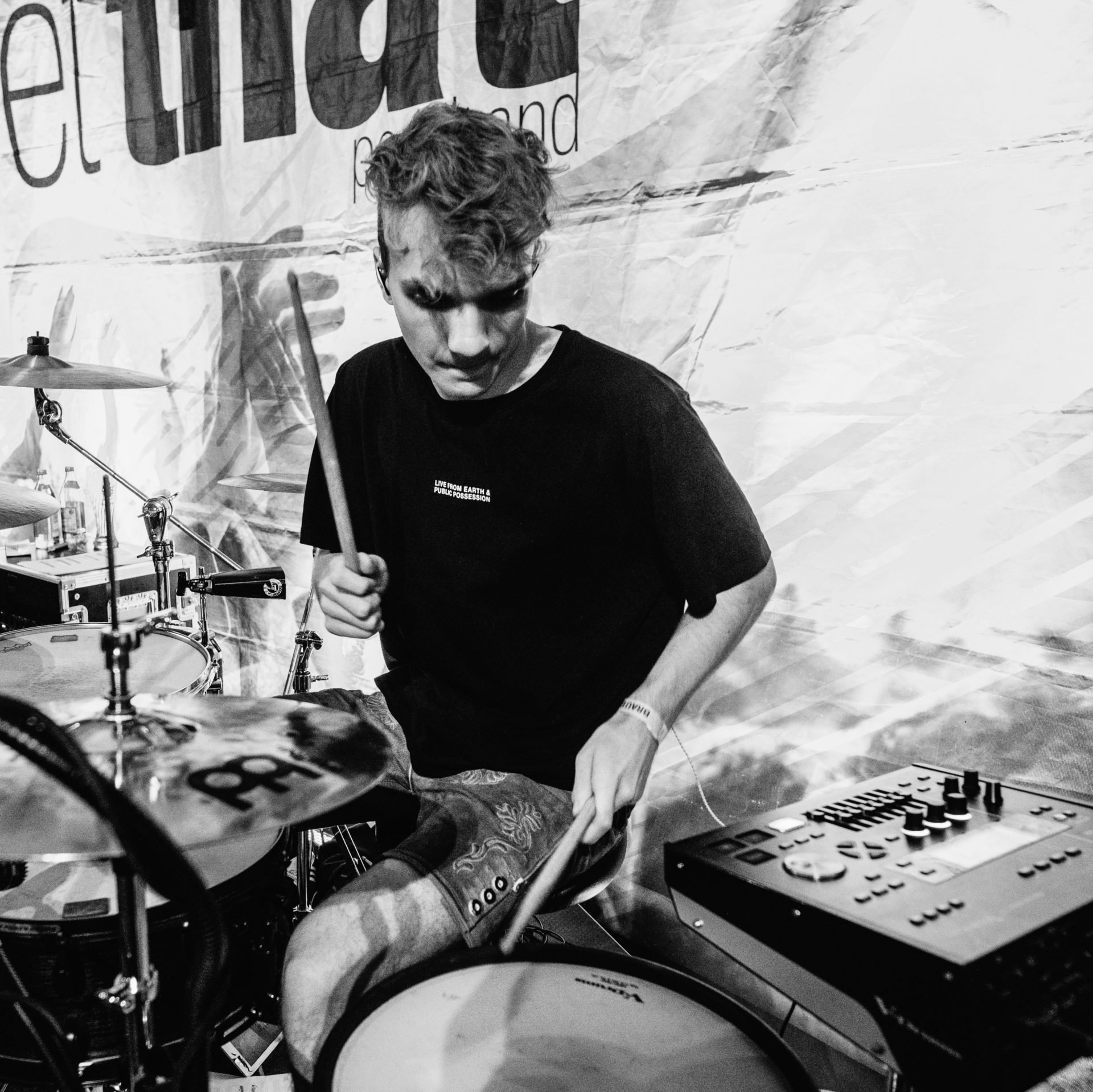 Ein junger Mann spielt Schlagzeug auf einer Bühne, umgeben von Musikgeräten.