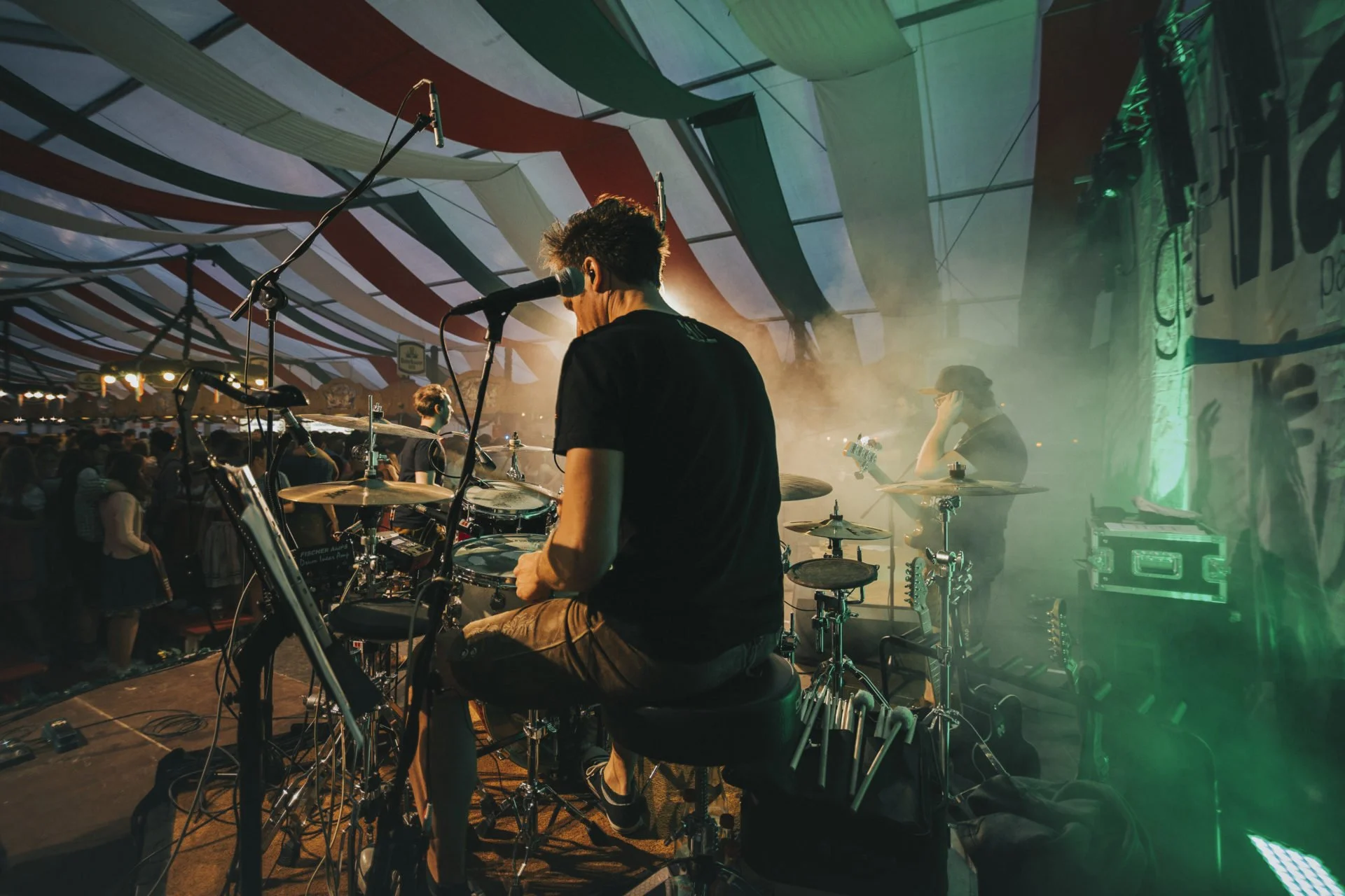 Musiker spielt auf einer Bühne bei einem Konzert, mit Publikum im Hintergrund, bunte Zeltdächer und Lichteffekte.