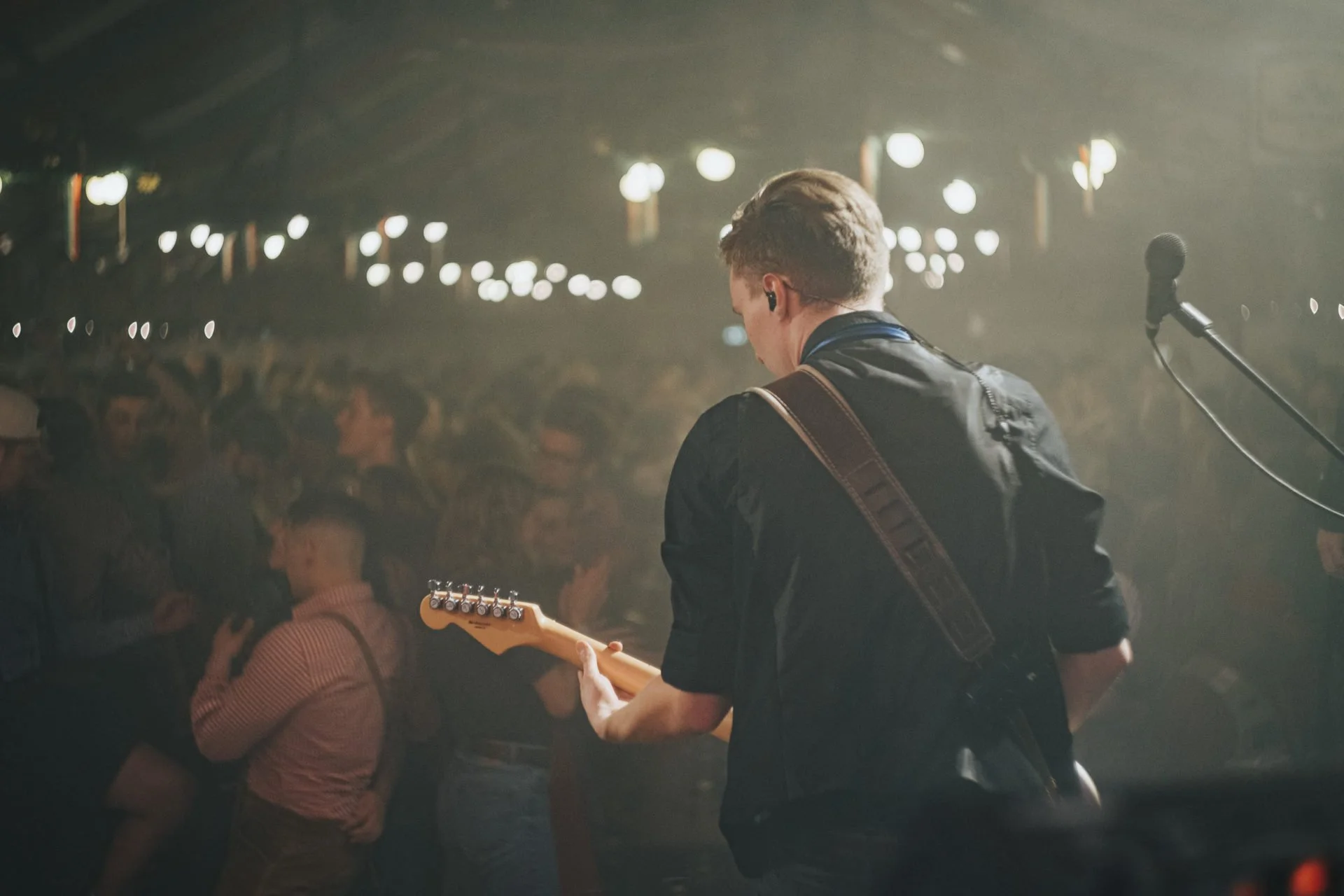 Ein Musiker mit E-Gitarre spielt auf einer Bühne vor Publikum bei einem Konzert.