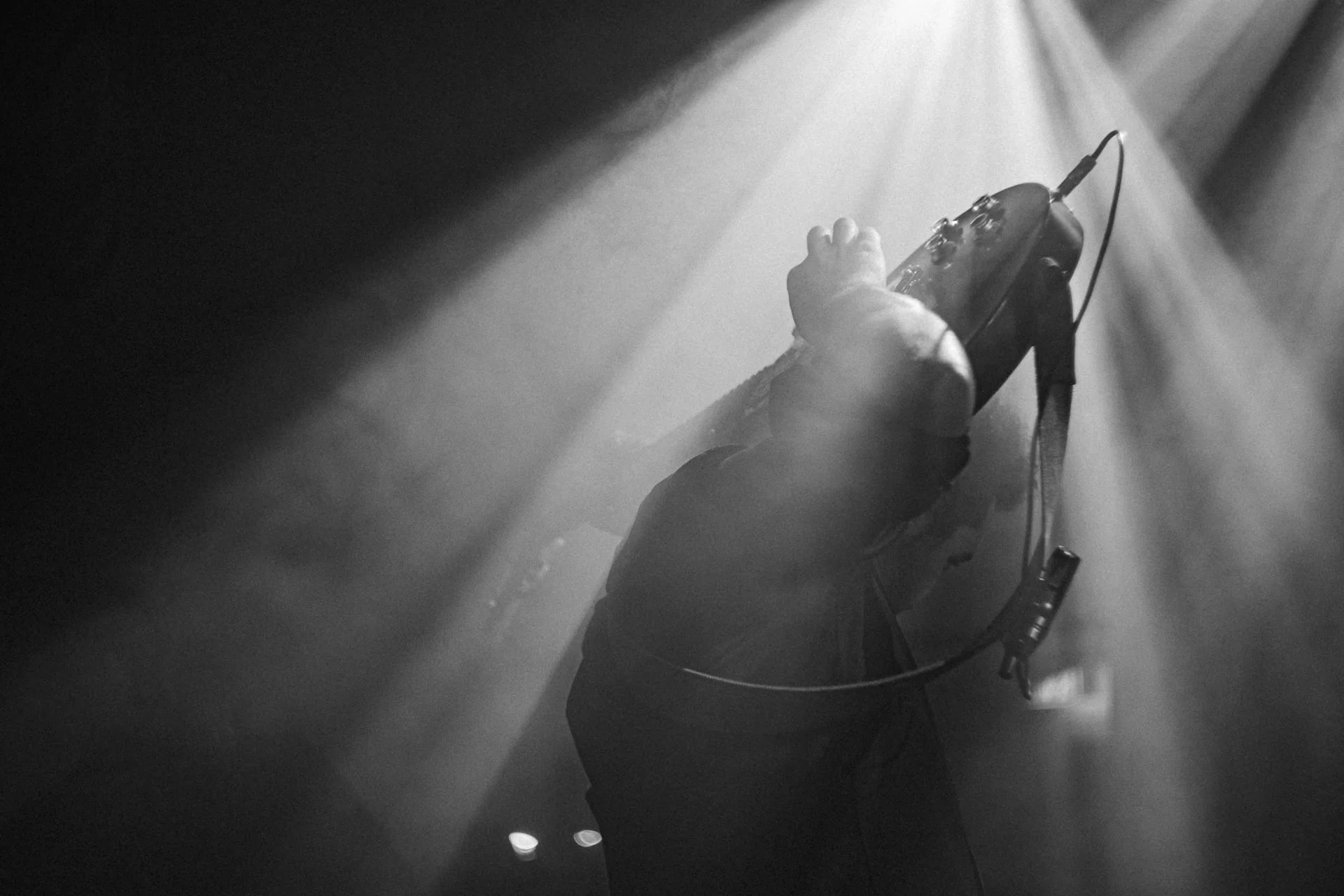 Ein Musiker spielt Gitarre auf einer Bühne, beleuchtet von Scheinwerfern, schwarz-weiß Foto.