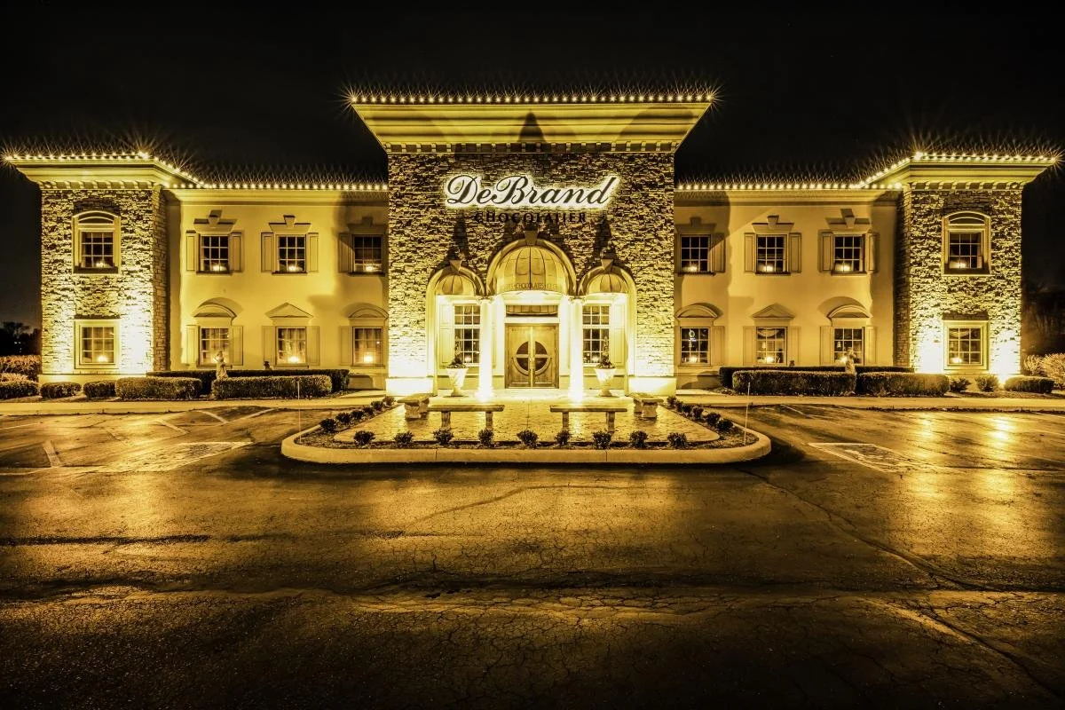 A well-lit, elegant building at night with the sign 'DeBrand Chocolatier' above the entrance.