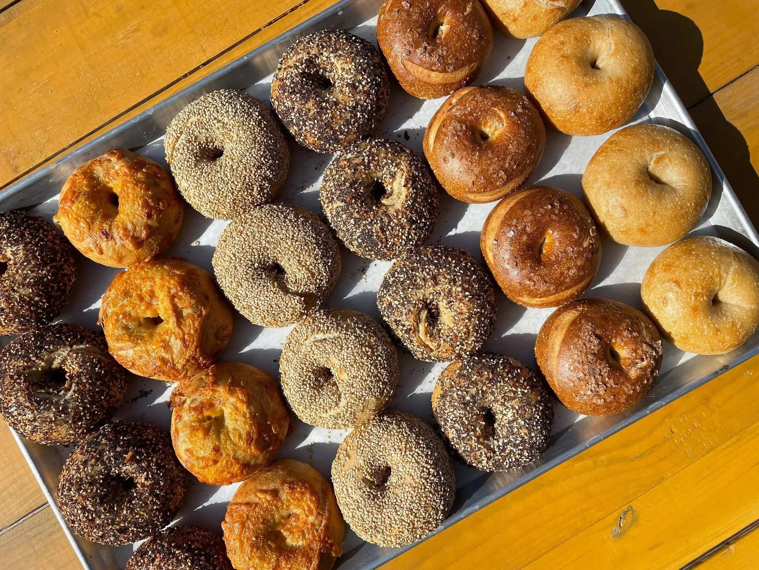A tray of assorted bagels including sesame seed, poppy seed, and plain bagels on a wooden table.