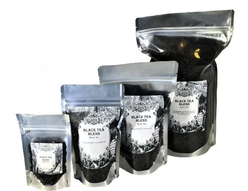 Four different sizes of black tea blend packages in resealable pouches, with a black liquid in a separate larger pouch at the back.