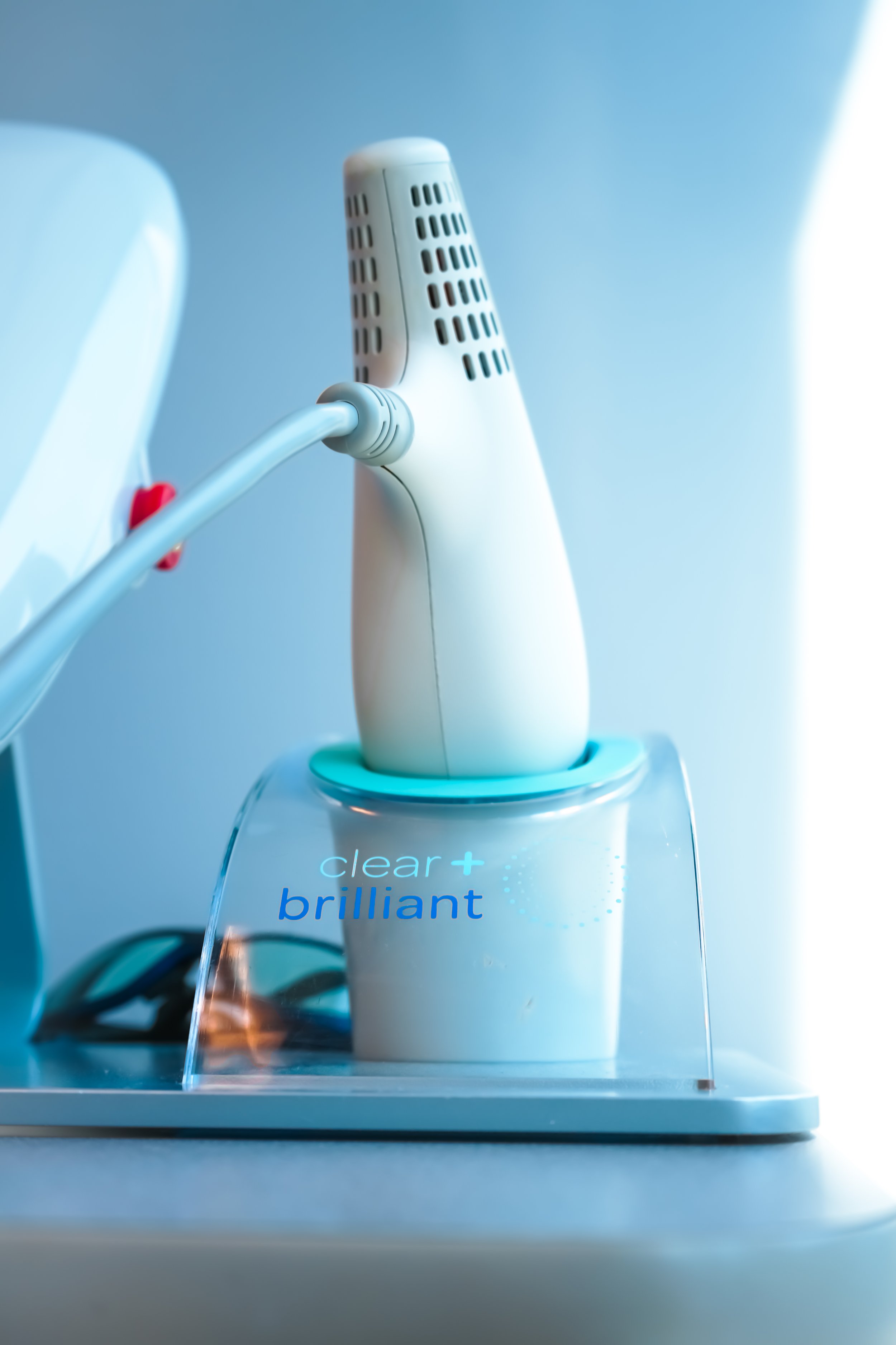 A close-up of a dental tool labeled 'clear+ brilliant' in a transparent container, connected to a device with an cable, on a clinical white surface.