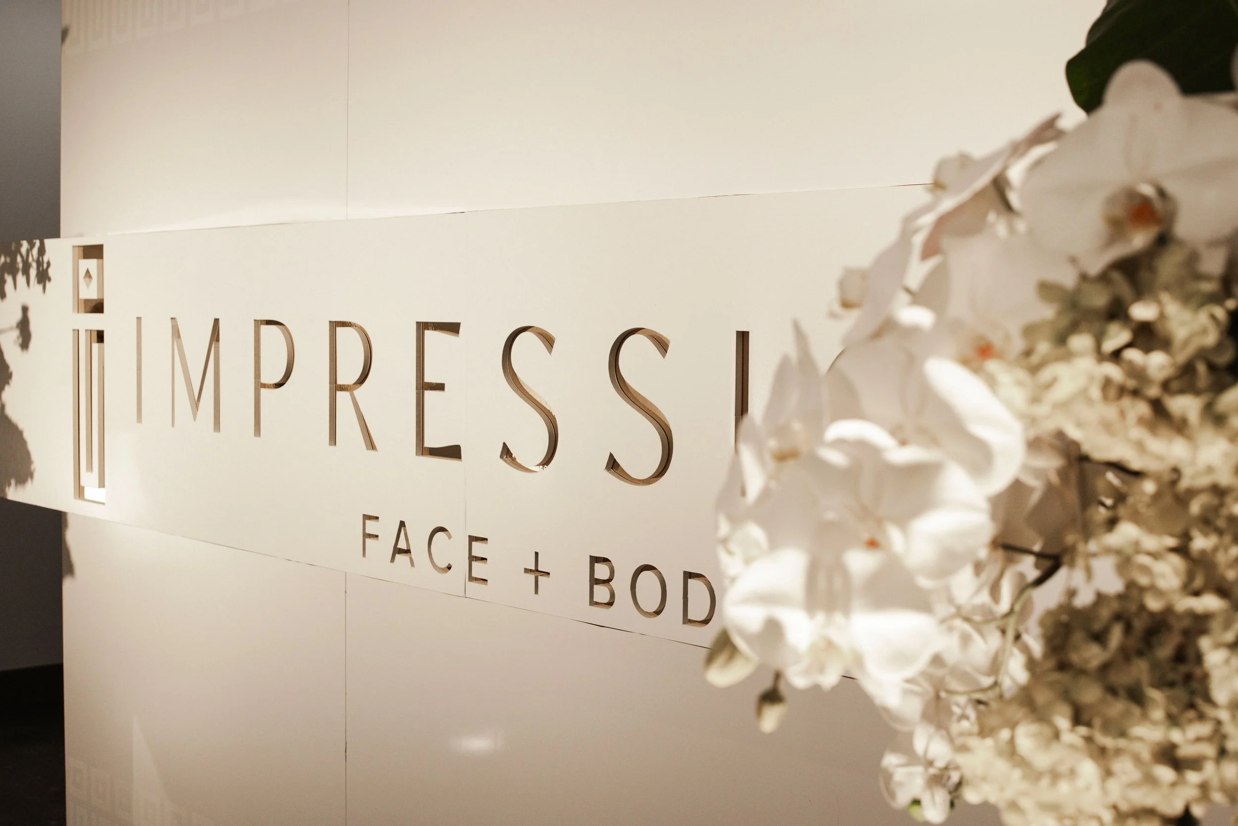 Sign reading 'IMPRESSI FACE + BODY' with a white floral arrangement on the right side.