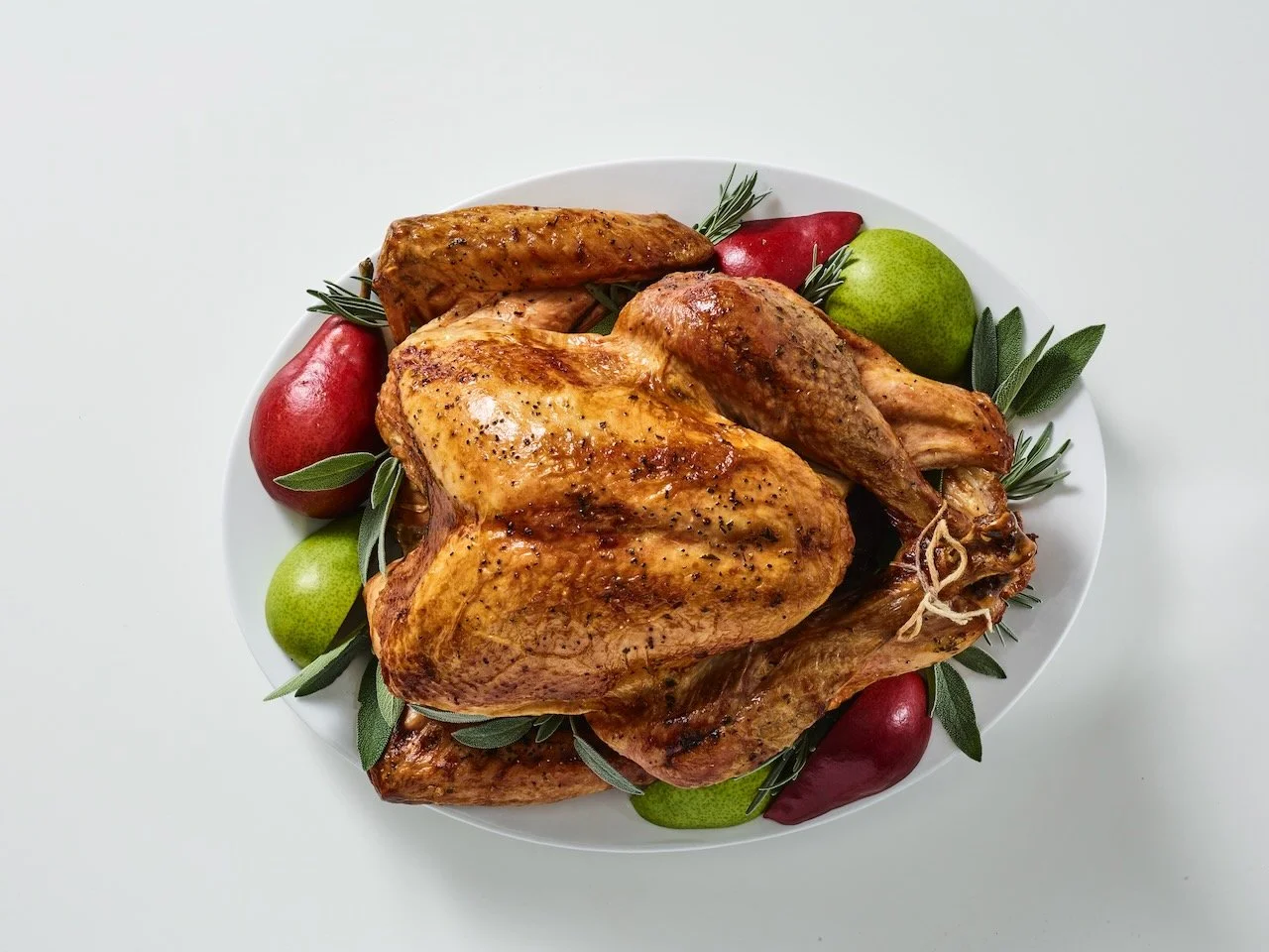 Roast chicken with herbs, garnished with red and green apples on a white plate.