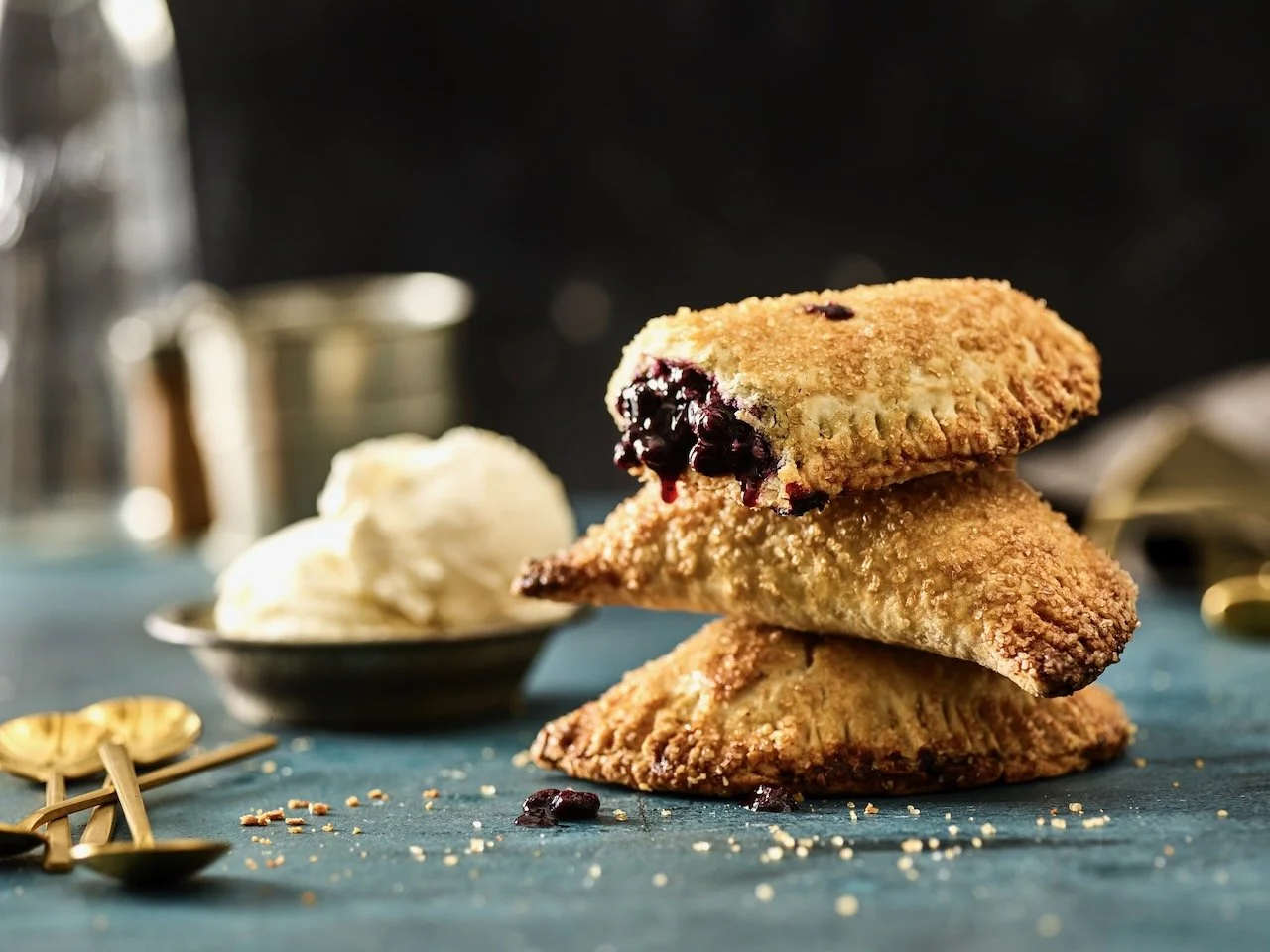 Stack of three cherry-filled pastry turnovers with a side of vanilla ice cream on a dark surface.