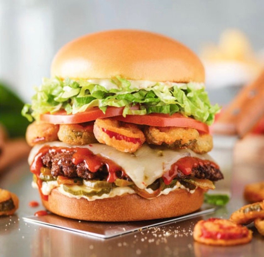 A close-up of a large, multi-layered burger with Red Robin burger with lettuce, tomato, fried onion rings, cheese,  hamburger patty, pickles, ketchup, and a sandwich bun styled by Beth Hawkins, of Hawkins and Co. A Denver, Colorado based food stylist