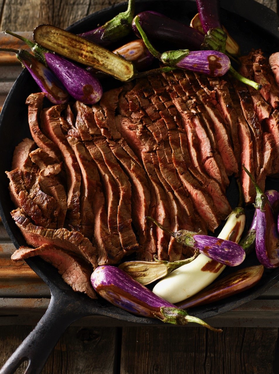 Sliced cooked steak in a cast iron skillet with roasted purple and white eggplants