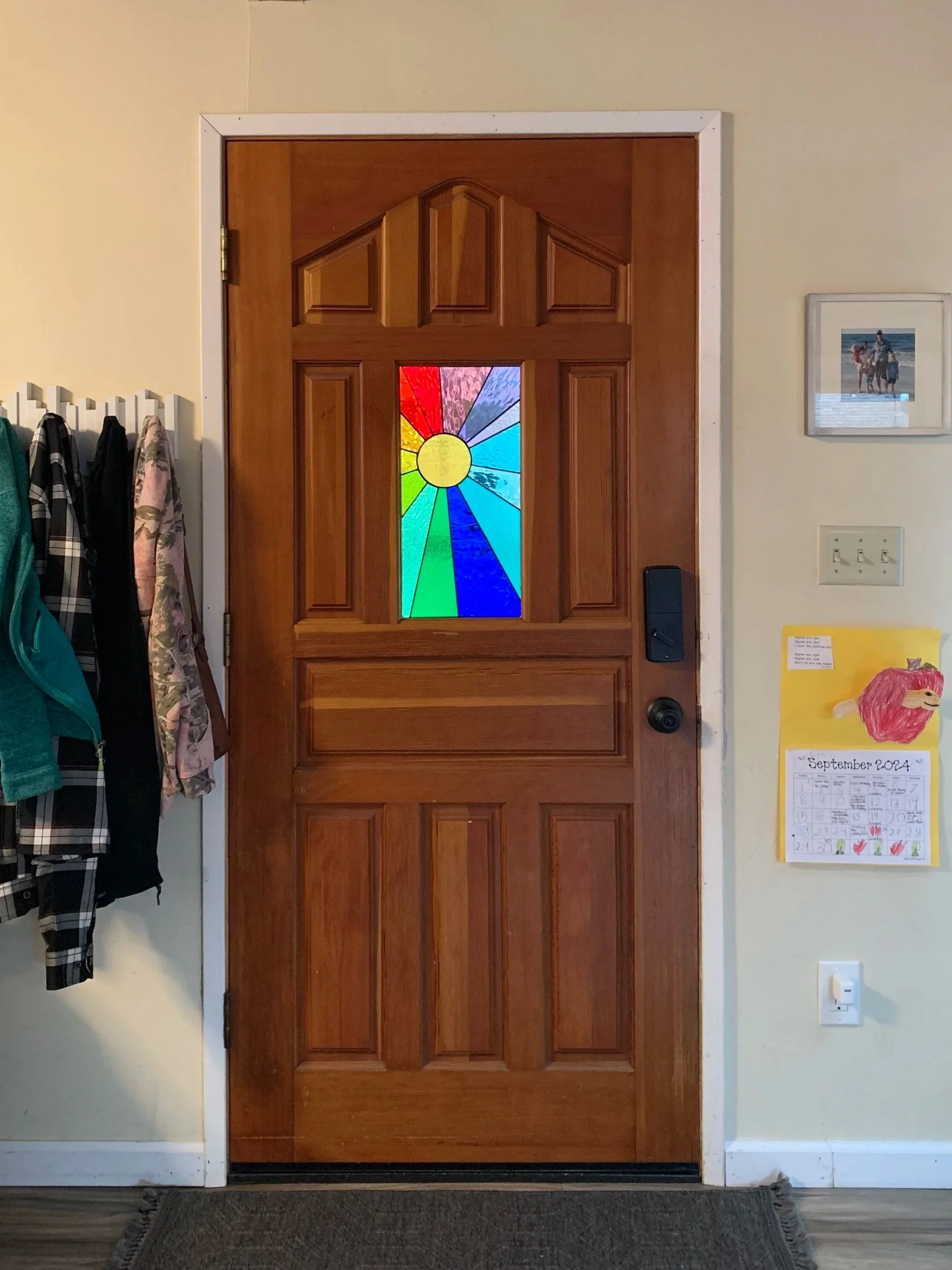 A stained glass panel of a rainbow colored sun installed in a wooden front door.