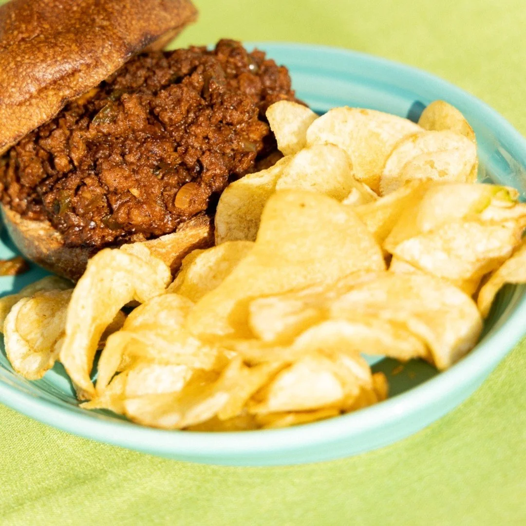 Fall head over heels for our Sloppy Joe, who's messy in all the right ways.
Seasoned ground beef or savory lentils (vegan) piled high on toasted sourdough, topped with creamy vegan coleslaw and crisp pickle slices. Served with your choice of pickle &