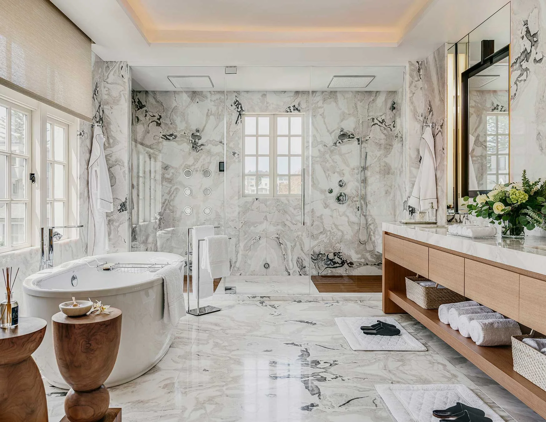 Bathed in natural light, this serene San Francisco primary bath is wrapped in walls of white marble. Teak wood slats underfoot and Kohler smart shower technology add to the spa-like experience.