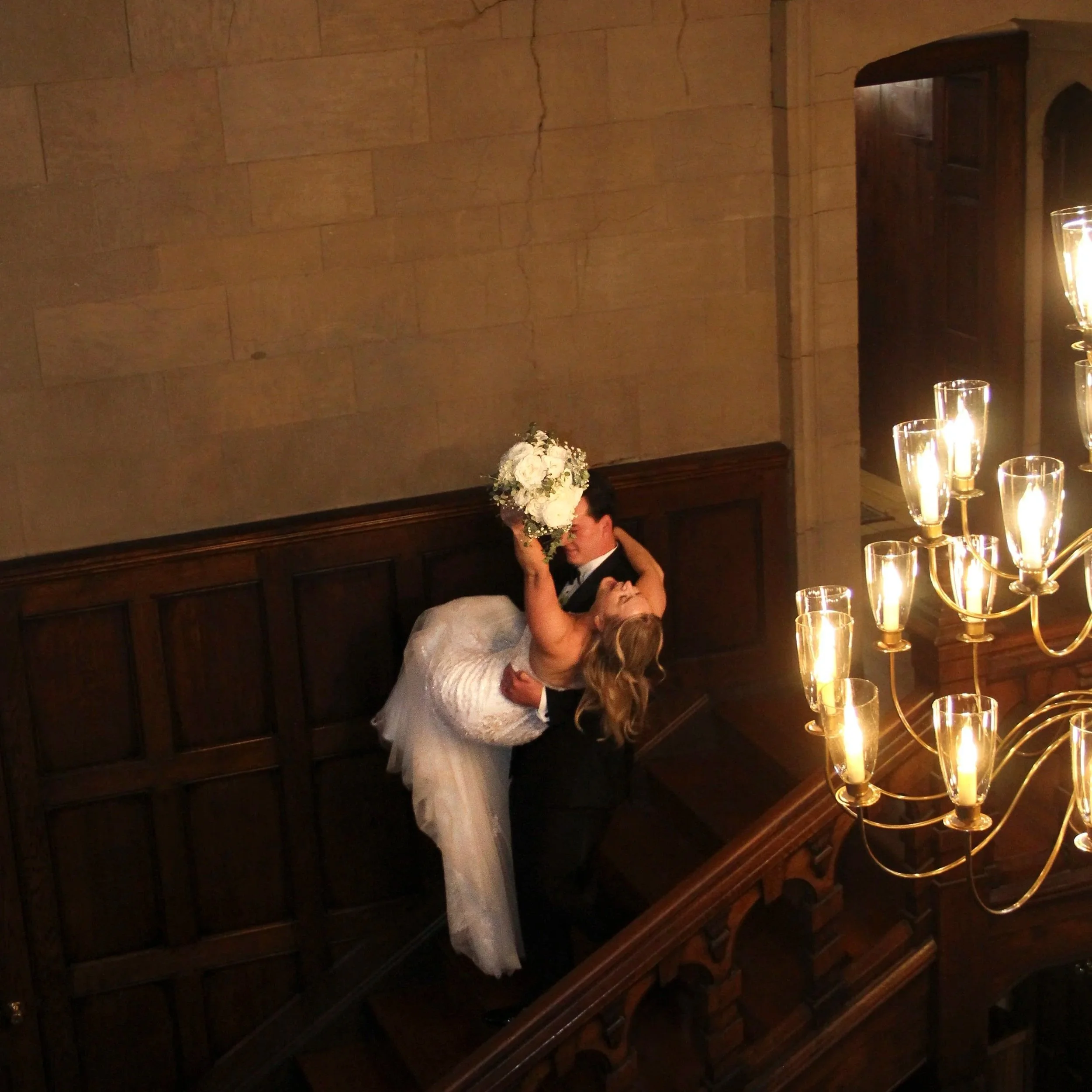 A couple dancing closely in a dimly lit room with a wooden wall and a chandelier with lit candles.