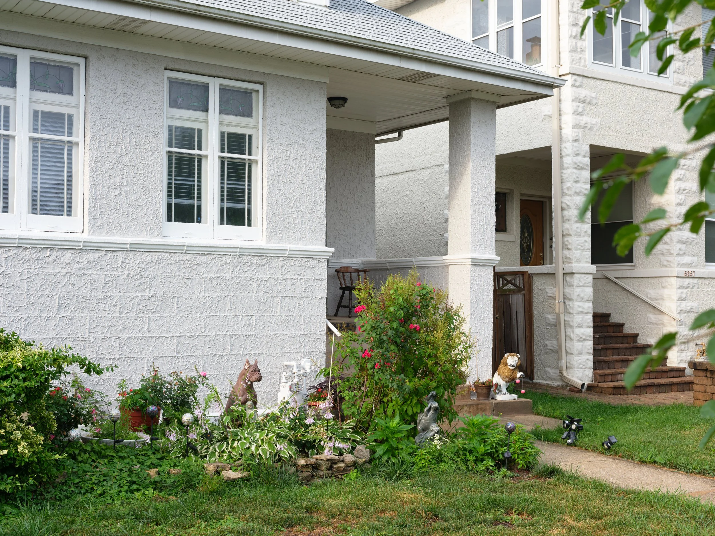 Front yard with garden, decorative statues, and a white house with steps and porch.