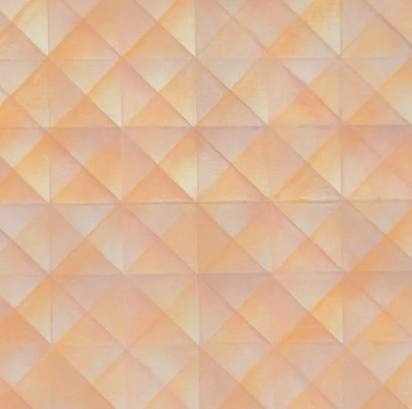 Close-up of a decorative wall with a repeating geometric pattern of pyramid-shaped tiles in shades of peach and beige.