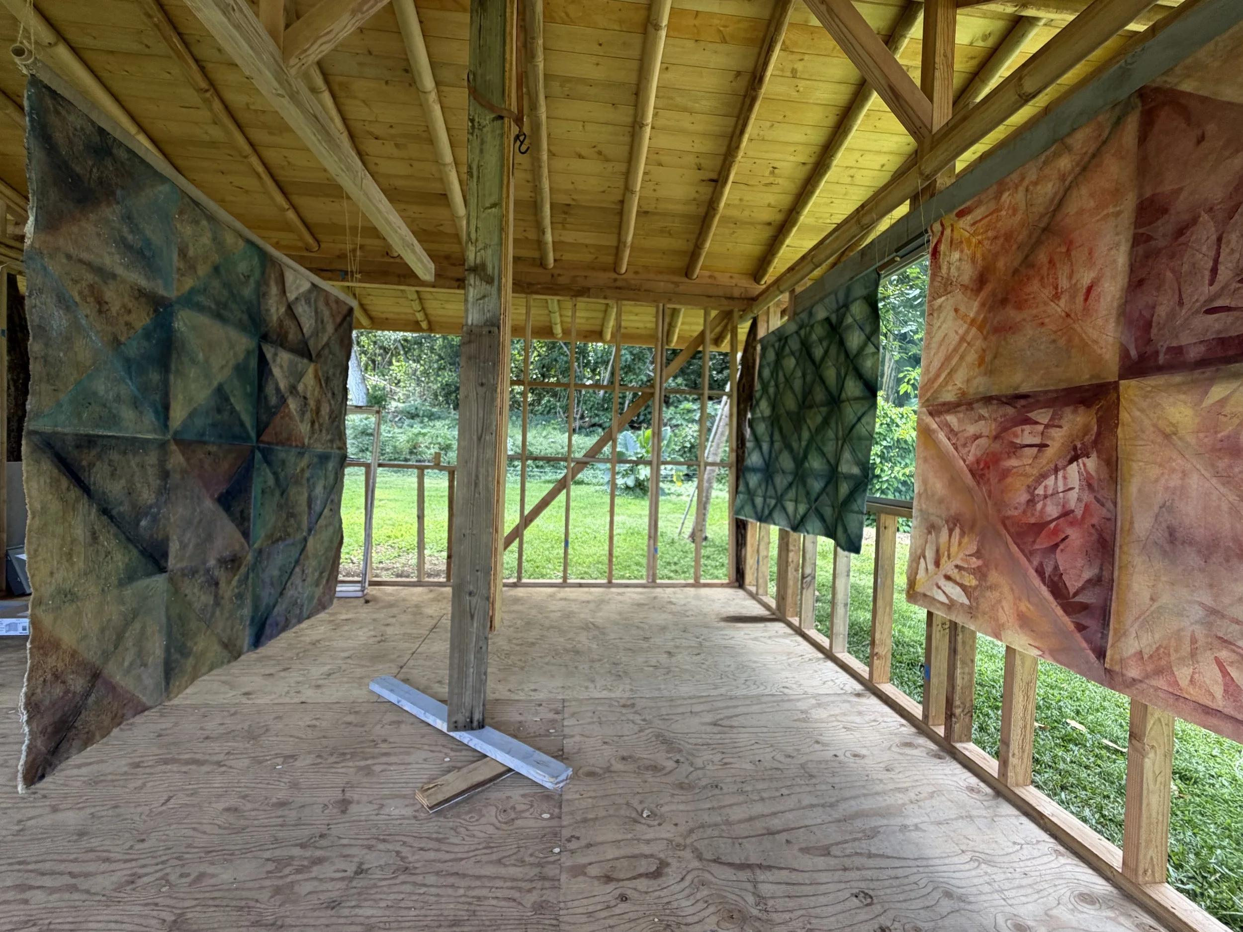 View of a wooden structure under construction with an unfinished interior, exposed beams, and hanging fabric or artwork panels with abstract designs.