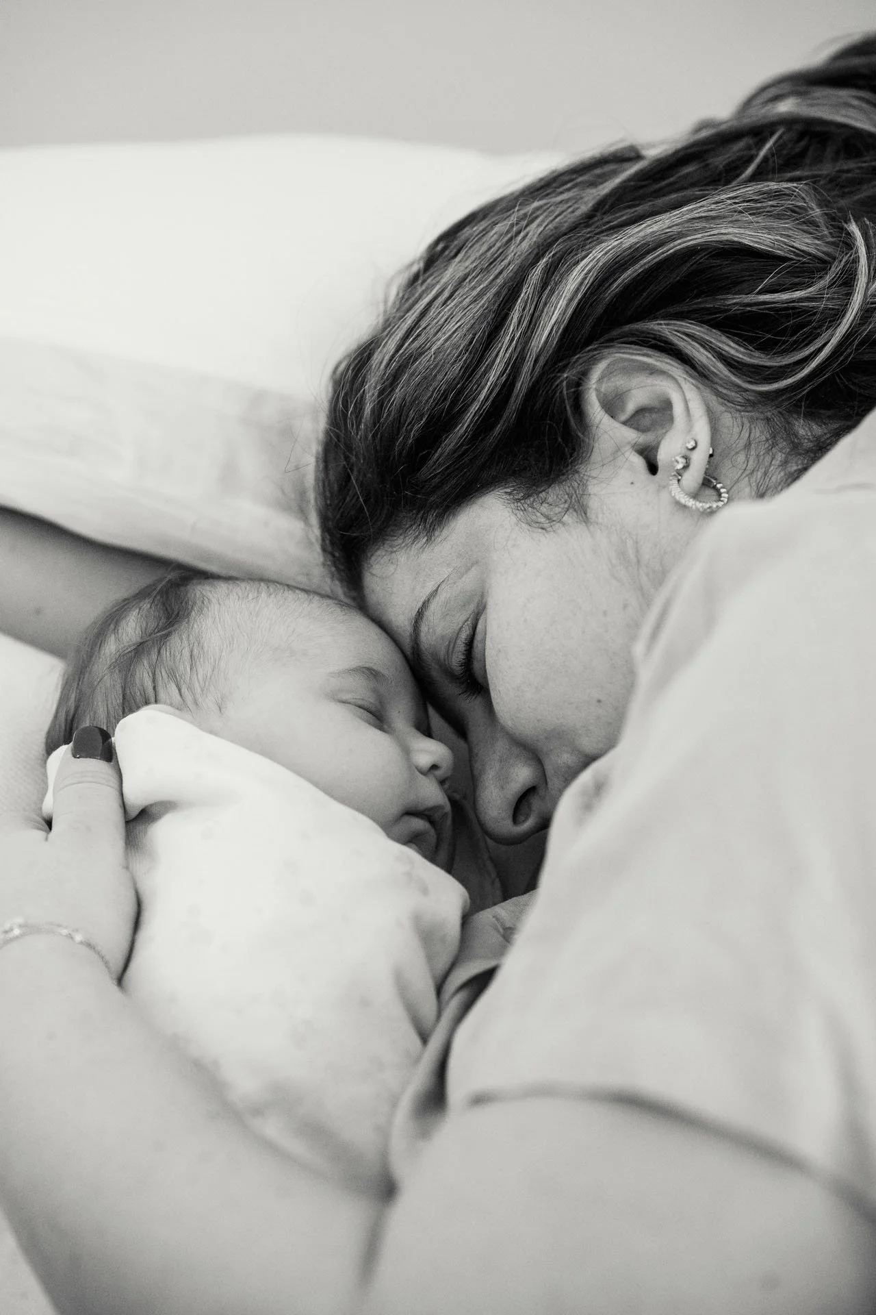 Black and white photo of a mother and her newborn baby lying on a bed with their foreheads touching, both sleeping peacefully.
