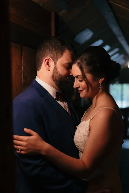 A bride and groom embracing each other, with eyes closed, in a warm indoor setting.