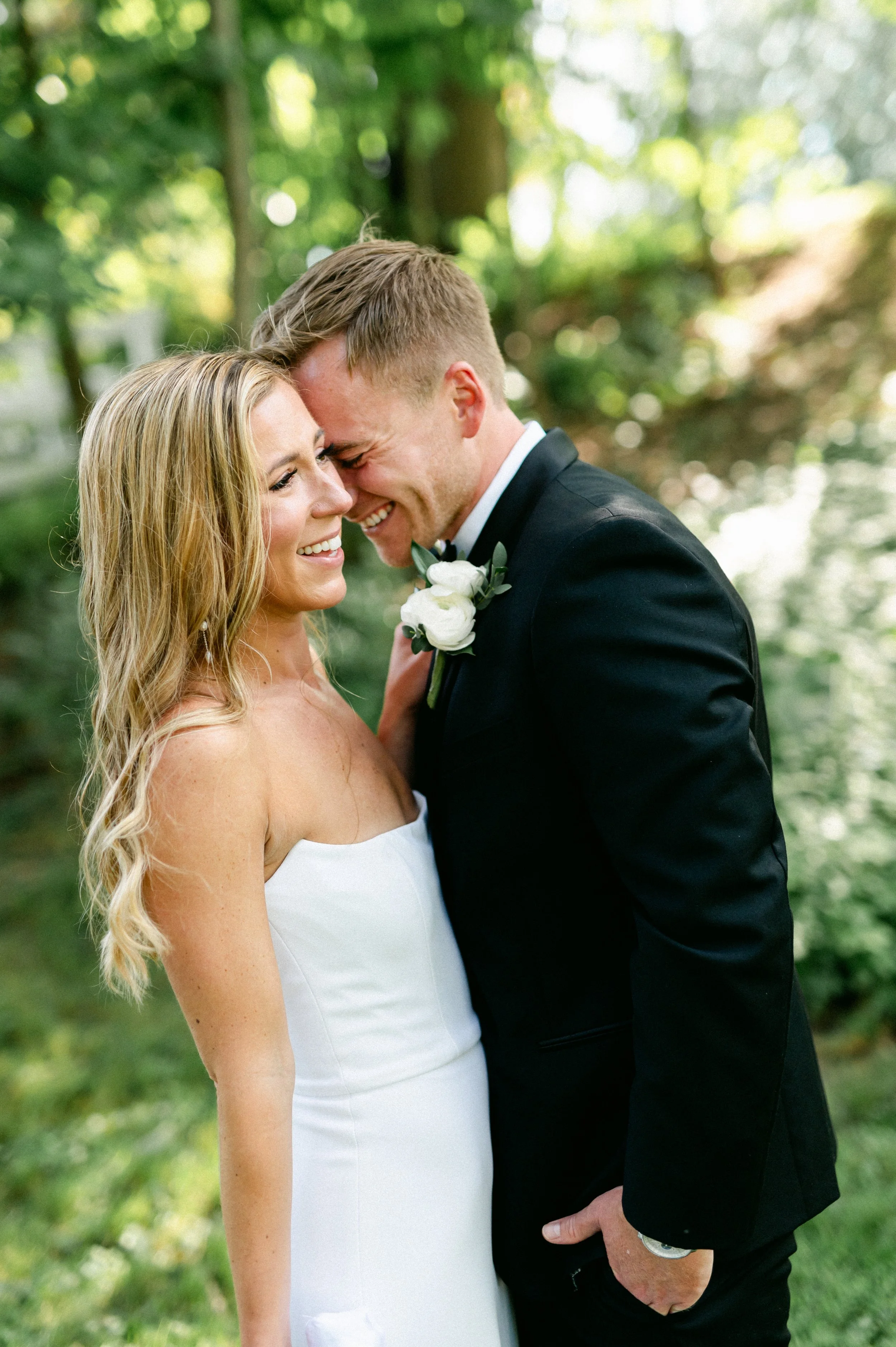 A bride and groom smiling and touching foreheads outdoors on their wedding day.