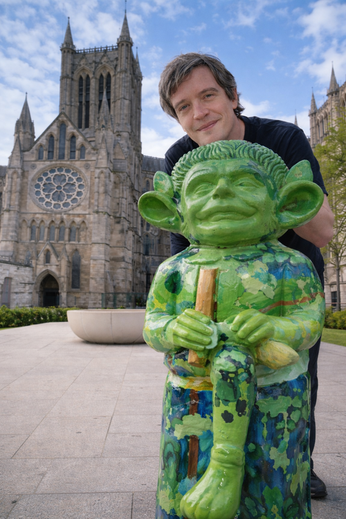 Stu standing behind a green imp and in front of Lincoln cathedral