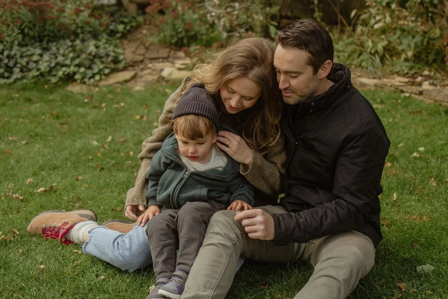 A family of three sitting on the grass in a backyard, embracing in their backyard in Evanston Chicago