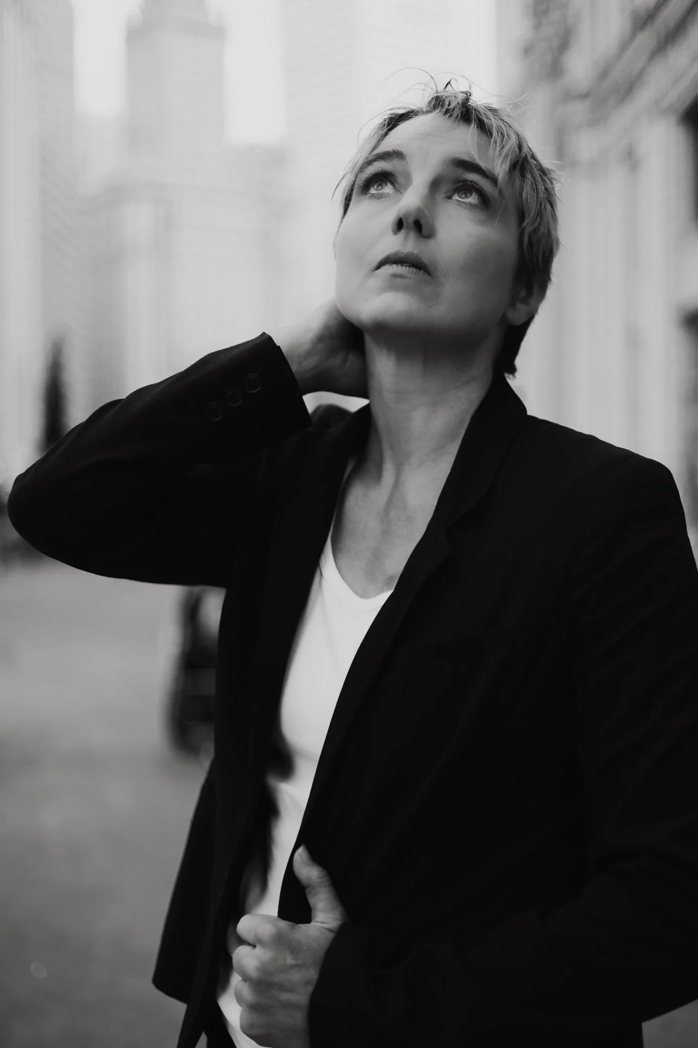 A woman with short, tousled hair looking upward with her hand on her neck in an urban setting by the Wrigley Building in Chicago Editorial style, in black and white.