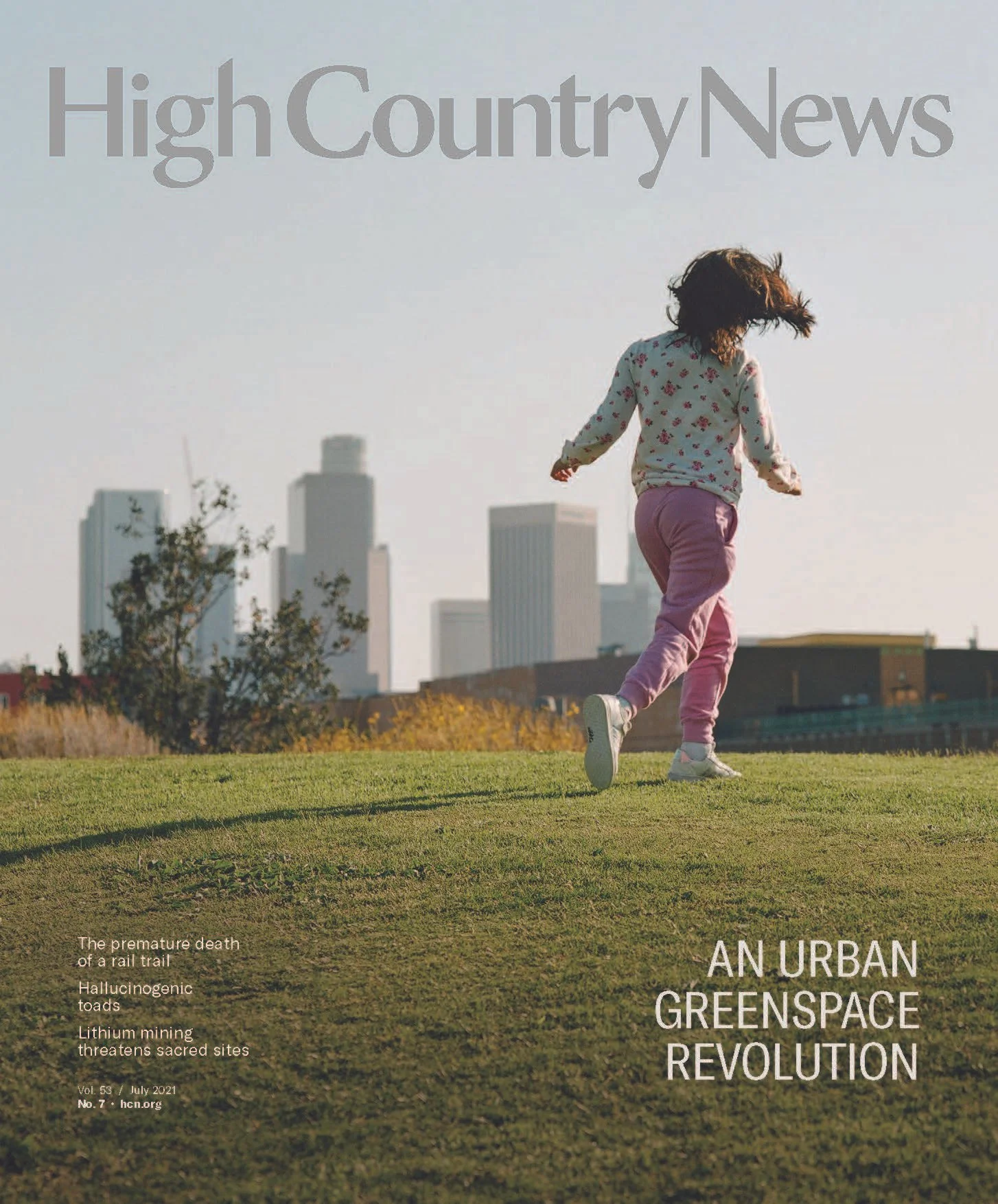 Magazine cover photograph of a girl running on a grassy hill with a city skyline in the background and the text 'High Country News' at the top and 'An urban greenspace revolution' at the bottom right.