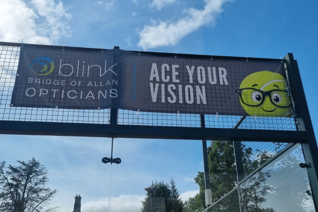 Padel court at Bridge of Allan Sports Club showing the new Blink banner which has the Blink logo with the words "Ace Your Vision" and our new glasses-wearing tennis ball "Boris Specker".