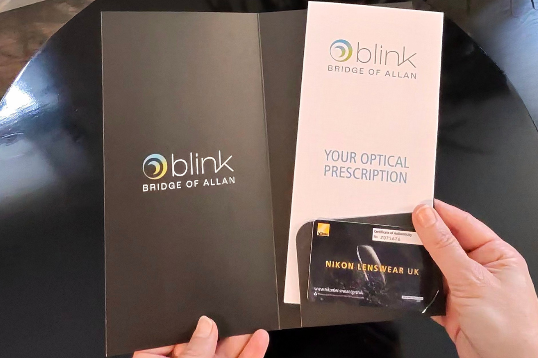 Hands holding a folder containing an optical prescription from Blink, Bridge of Allan. The folder also contains a Nikon Lenswear UK card.
