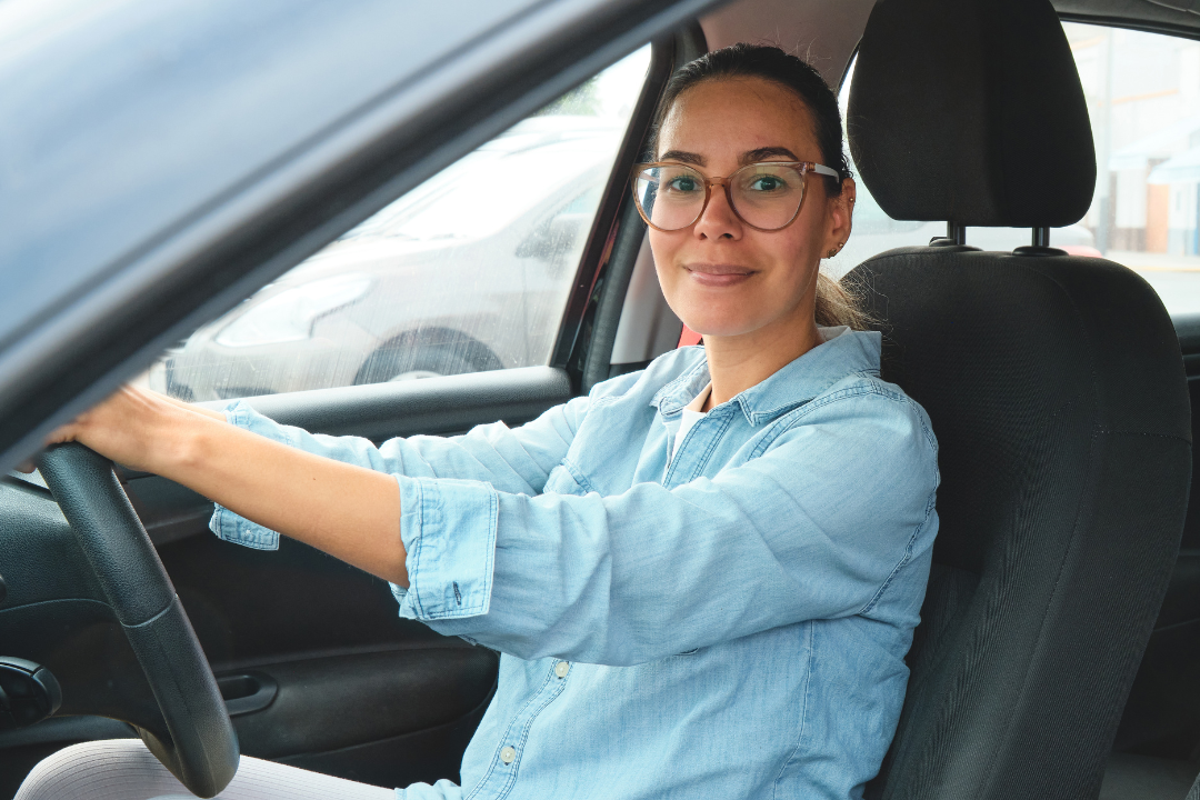 Female Driver wearing glasses sitting behind the wheel of a small car in the UK.