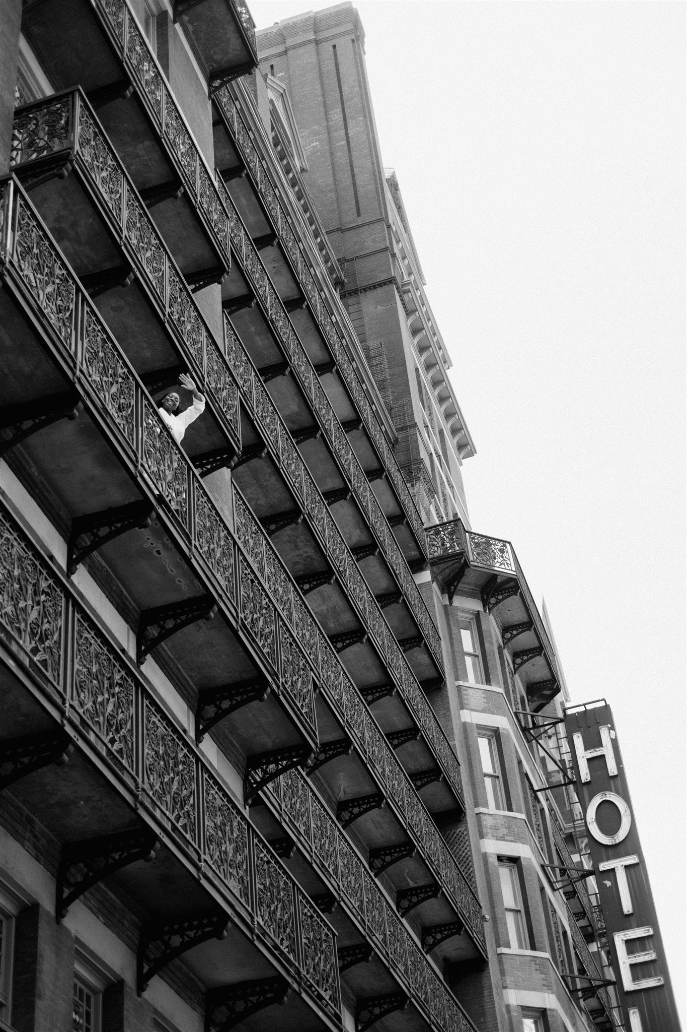 Black and white photo of a multi-story building with ornate iron balconies and a large vertical hotel sign.