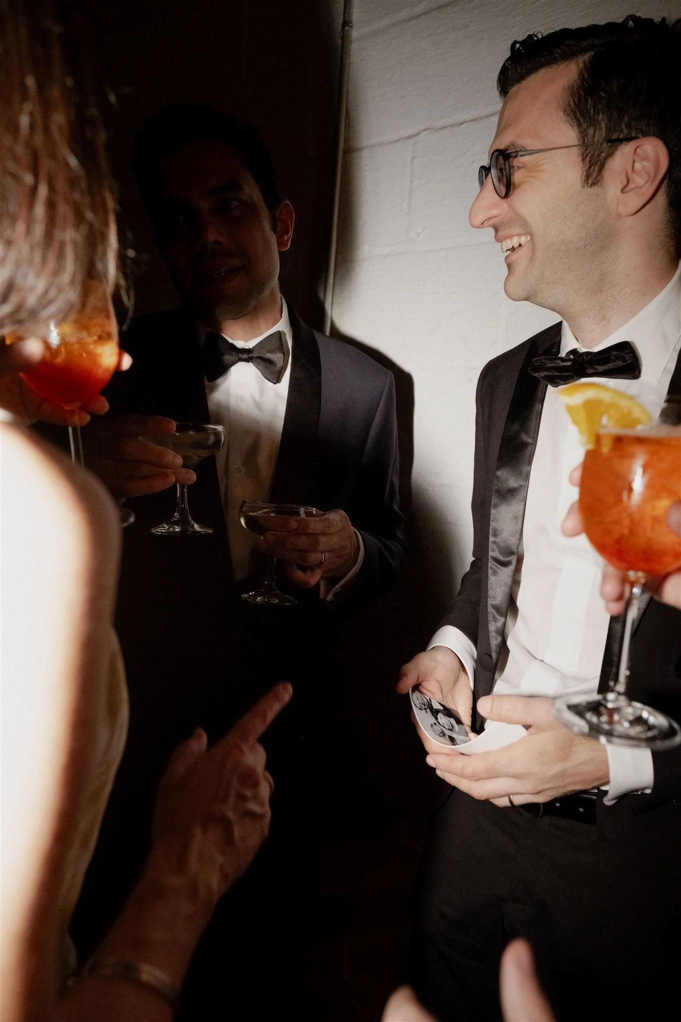 Group of people in formal attire at a cocktail party, holding drinks, engaging in conversation, and smiling.