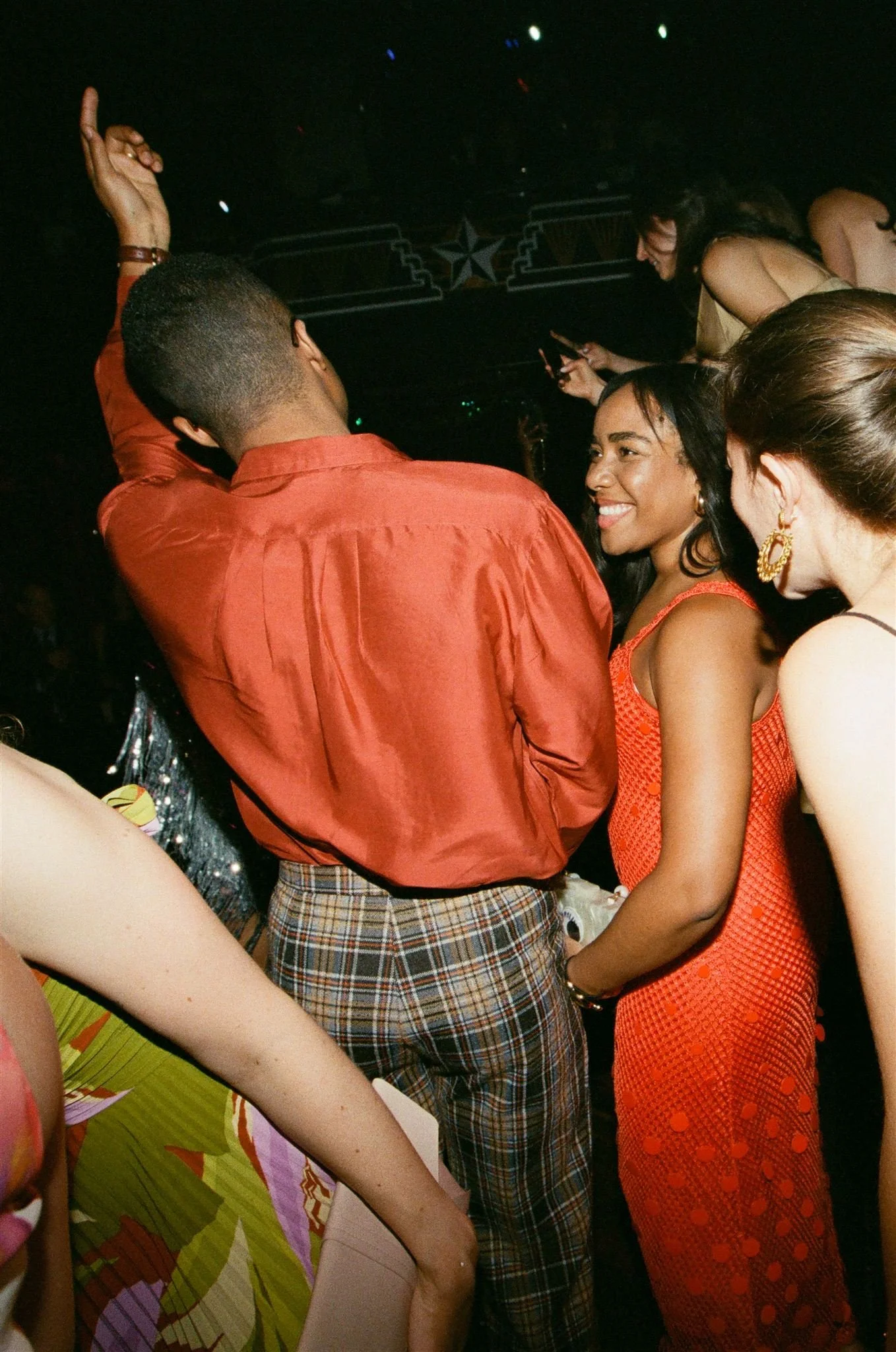 People dancing and socializing at a party or nightclub with low lighting and colorful lights.