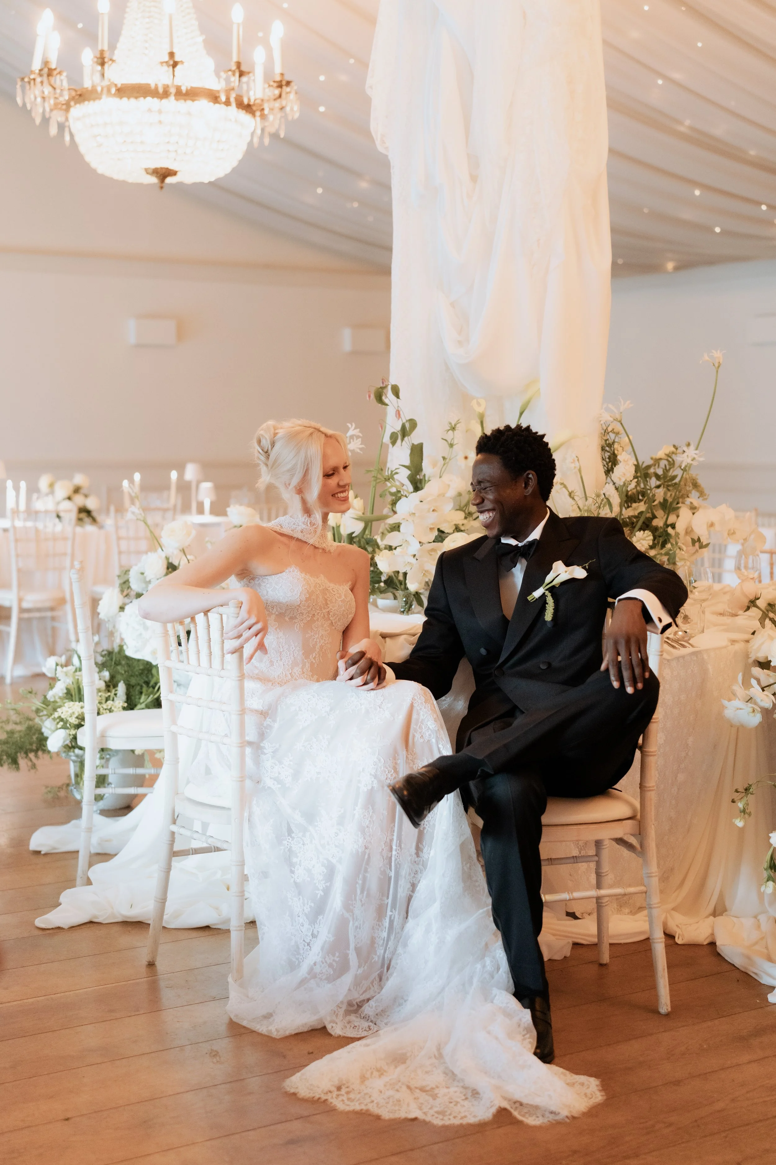 Bride and groom seated together laughing during an editorial wedding setup at Iscoyd Park, styled with soft florals, draping, and candlelight