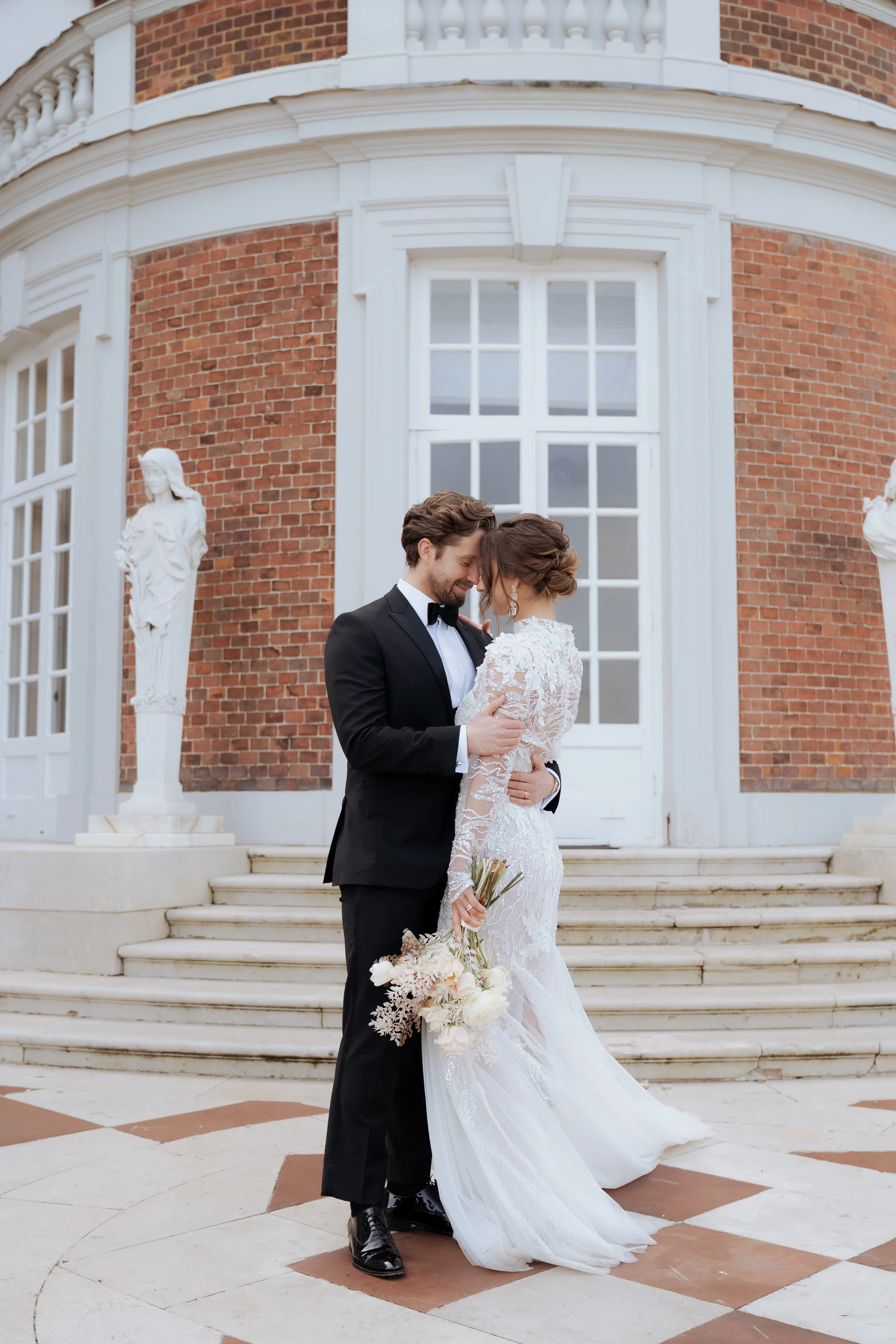 Bride and groom embracing on the steps of a grand Staffordshire wedding venue with classic architecture, soft natural light and elegant editorial wedding styling.
