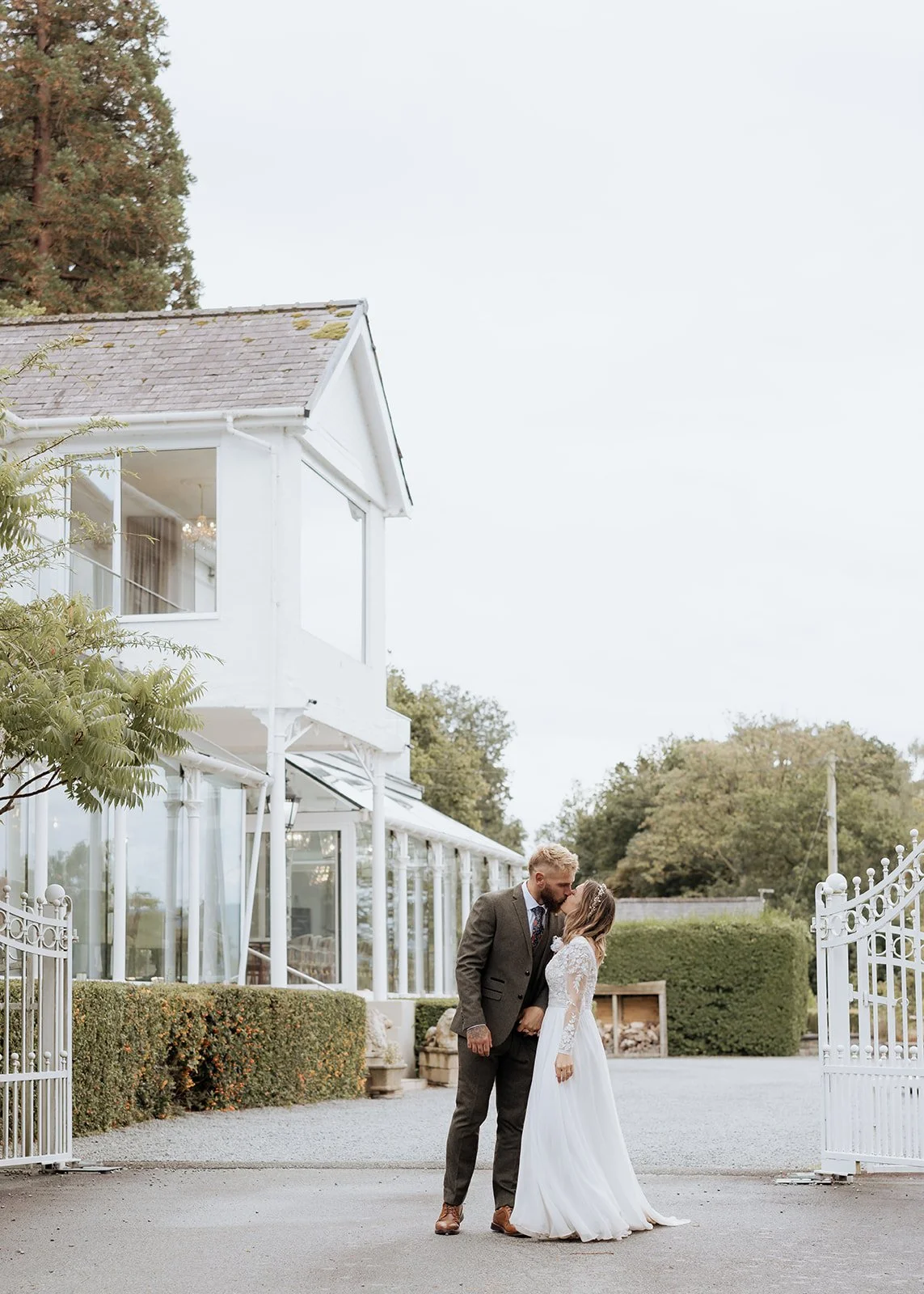 ntimate destination wedding moment of a couple kissing outside a luxury countryside estate, captured in a soft editorial photography style.