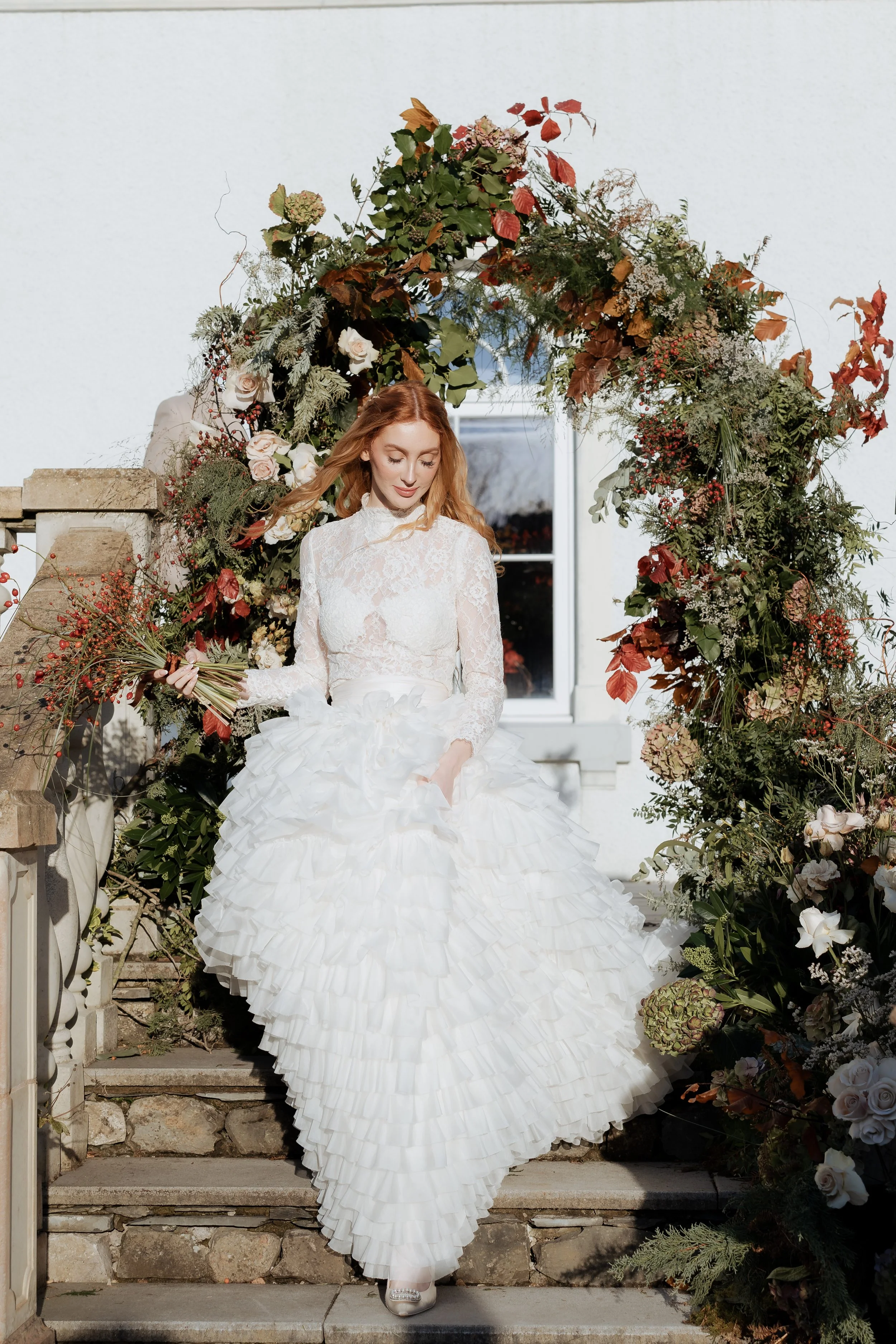 Editorial bridal portrait framed by a floral arch, photographed in a soft, natural style with an emphasis on elegance and atmosphere
