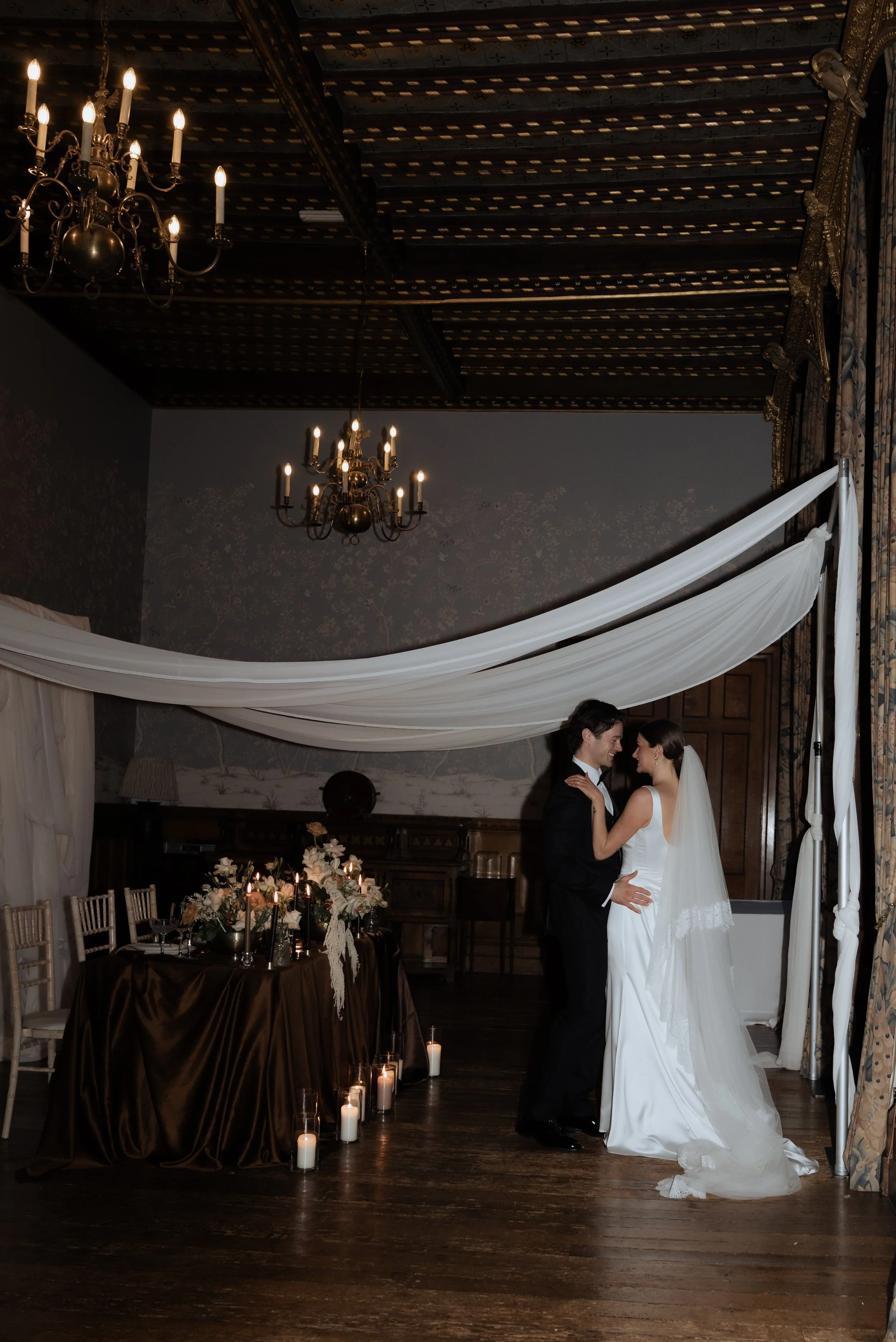 Bride and groom sharing a quiet moment beneath draped fabric and candlelight during an editorial wedding at Soughton Hall
