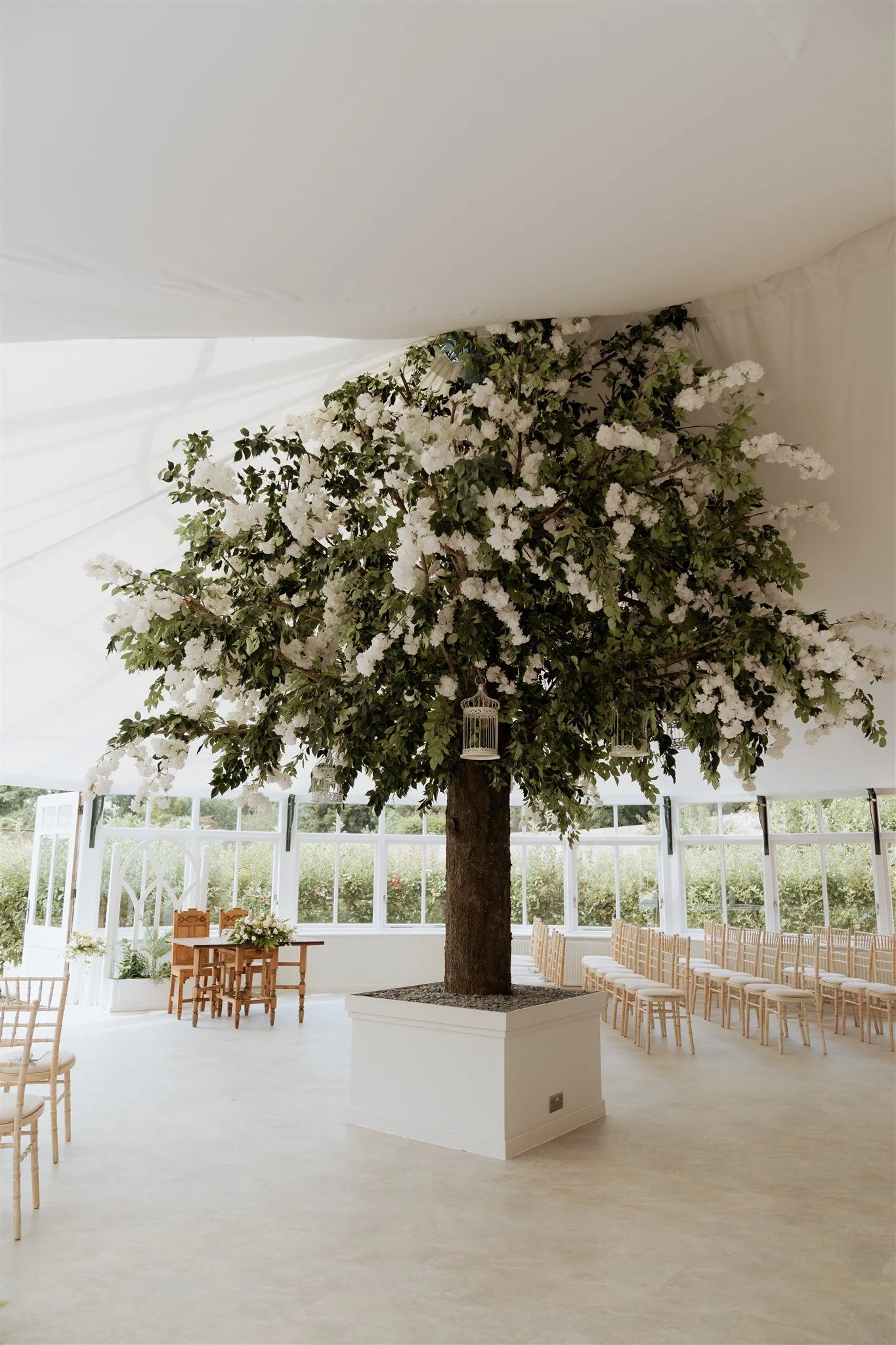 Elegant glasshouse ceremony setup at Combermere Abbey featuring floral tree styling and refined wedding décor.