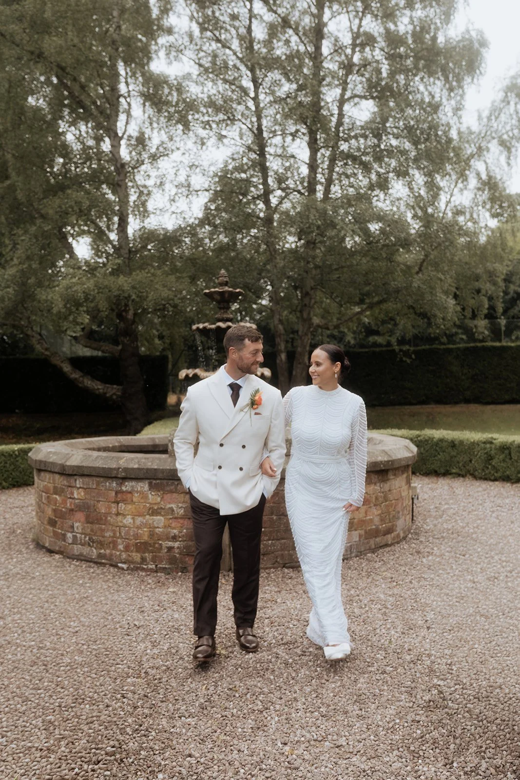 Bride and groom walking together by the fountain at Soughton Hall during a luxury Cheshire wedding
