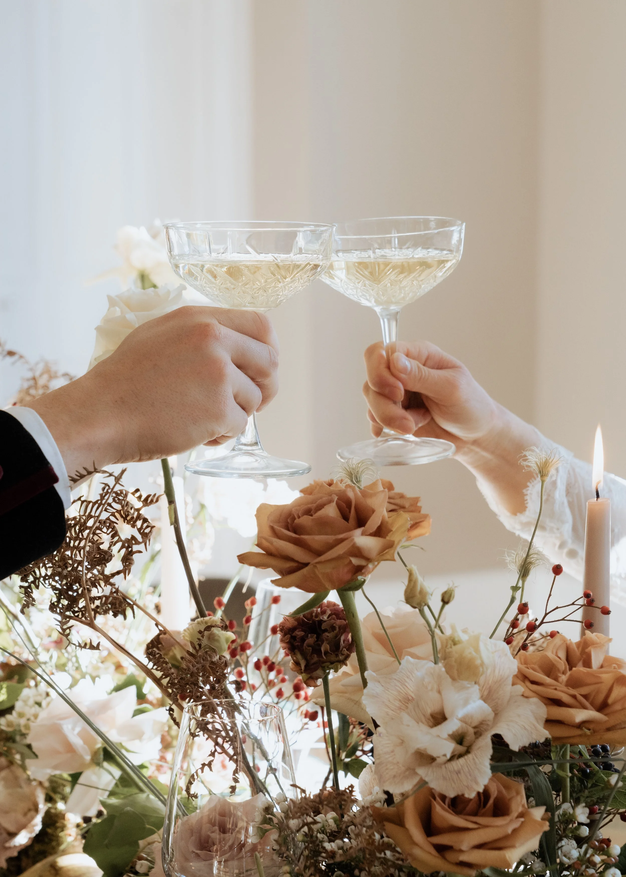 Intimate editorial wedding moment capturing a champagne toast above soft floral table styling