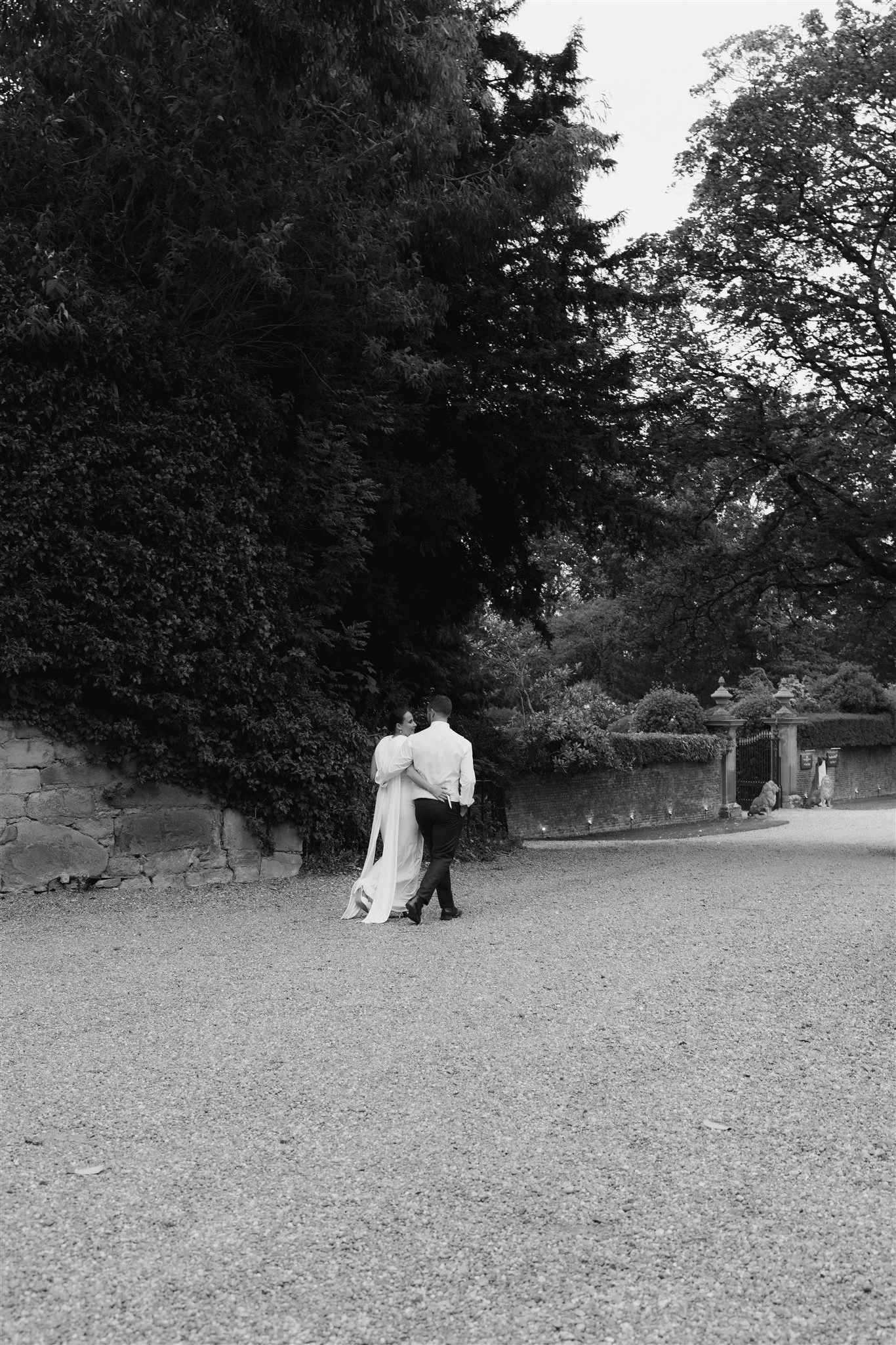 Black and white wedding photograph of a bride and groom walking together through the grounds of Soughton Hall, captured in a timeless editorial style