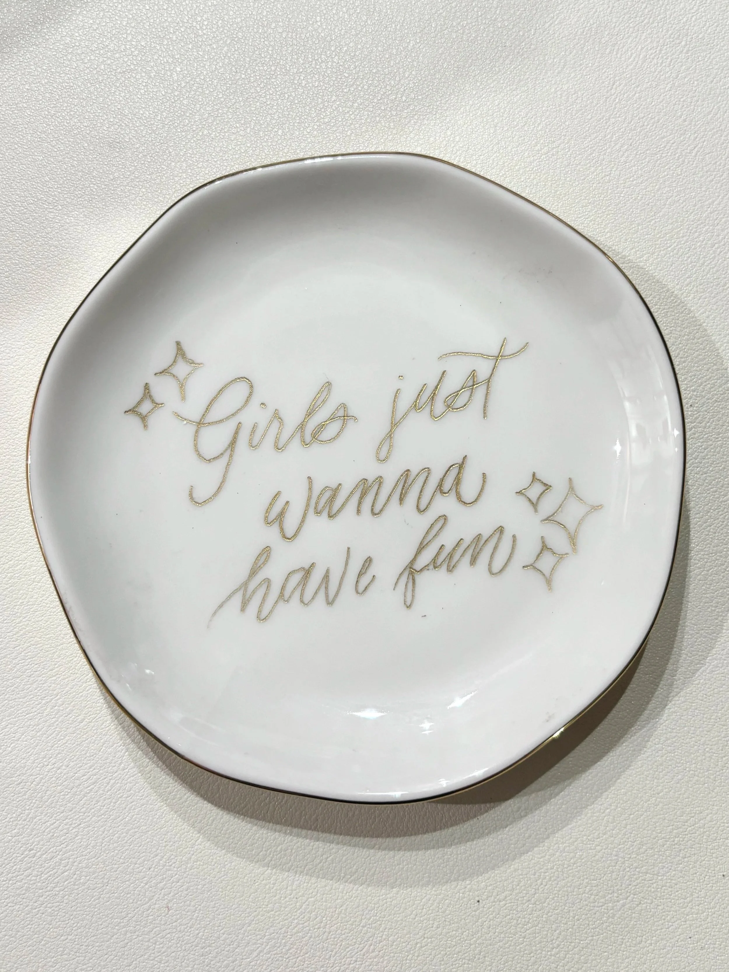 A white ceramic dish with gold edges and gold handwritten-style text that reads, 'Girls just wanna have fun,' with small star illustrations around the text.