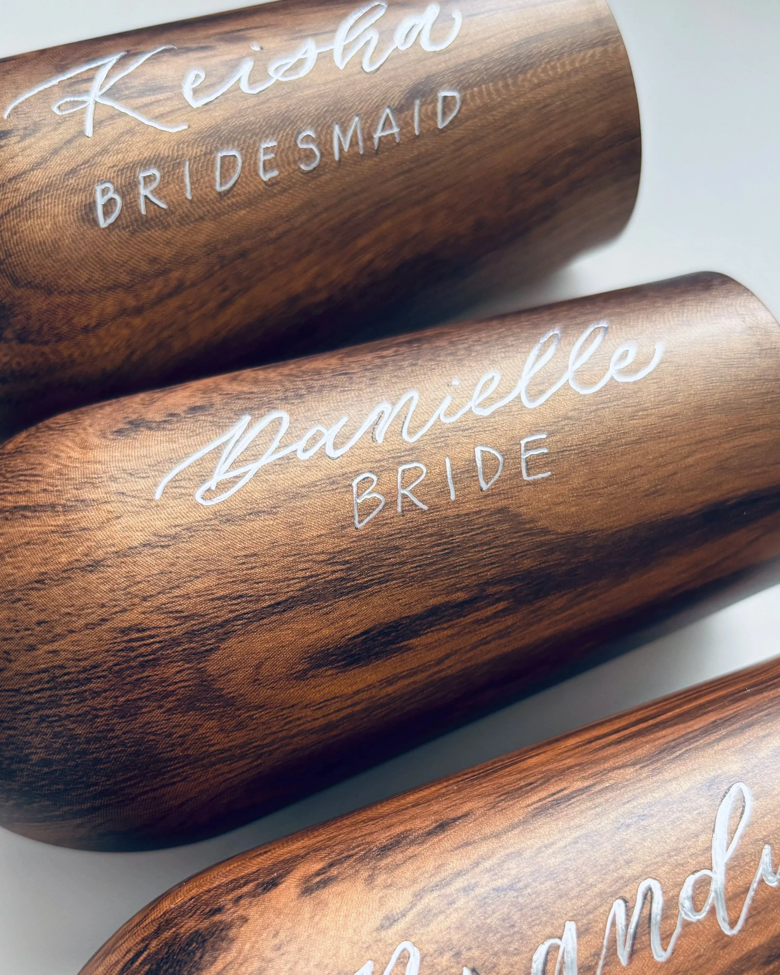 Close-up of engraved wooden champagne flutes with names and titles, including 'Keisha BRIDESMAID' and 'Danielle BRIDE'