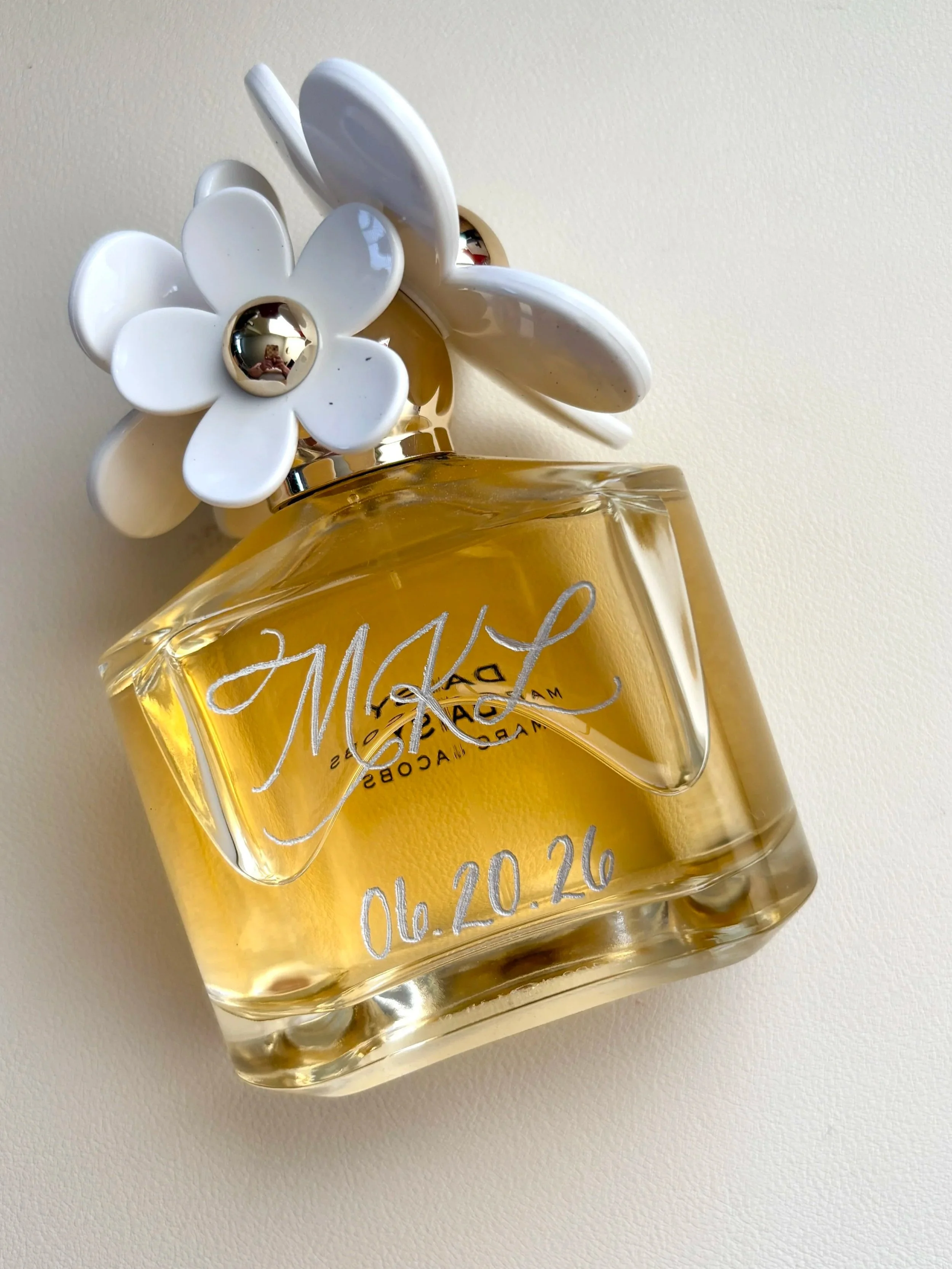 A bottle of Marc Jacob's "Daisy" engraved in silver with the letters "MKL 06.20.26"